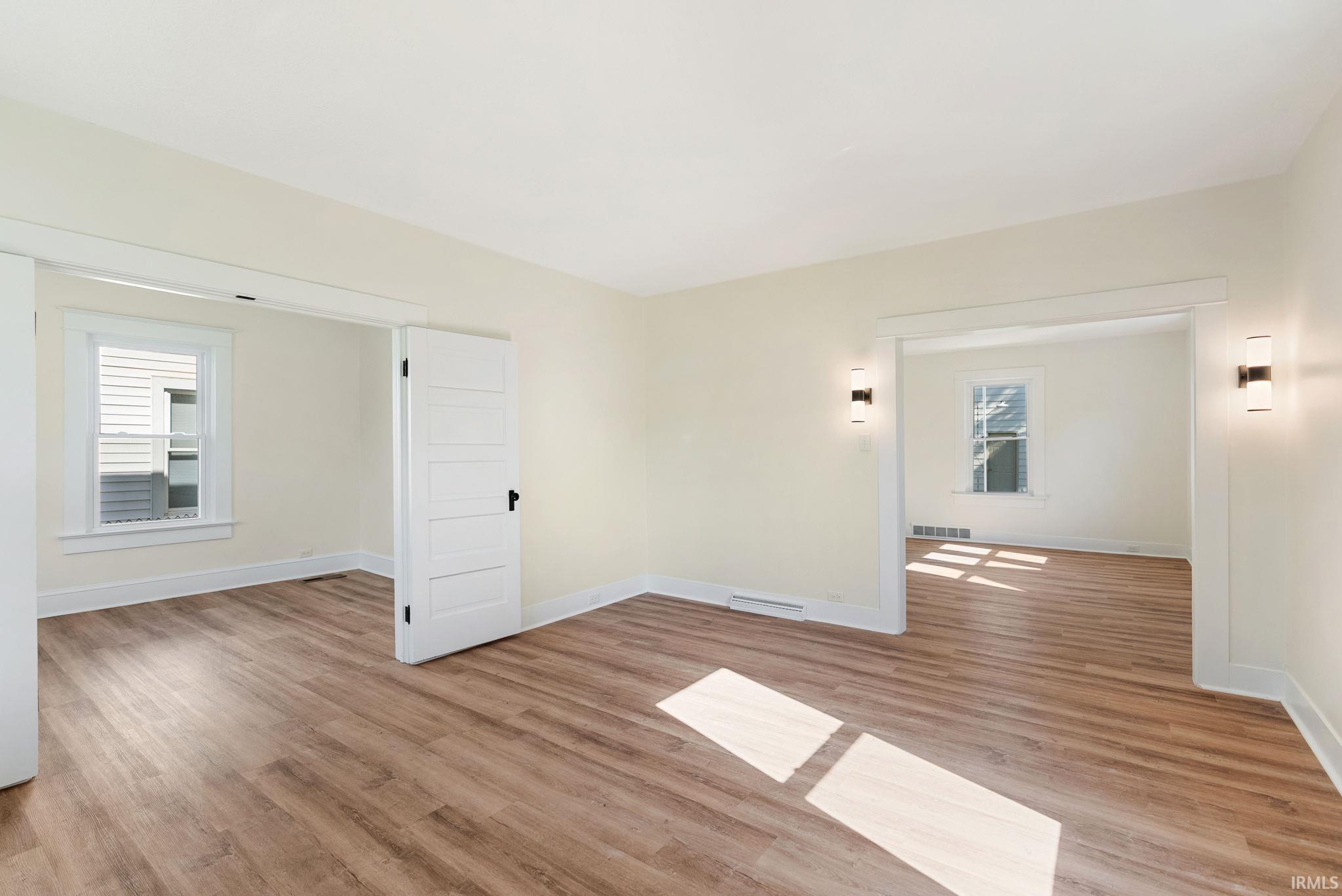 Interior space featuring wood-finish flooring, light-toned walls, white trim, and two wall-mounted light fixtures