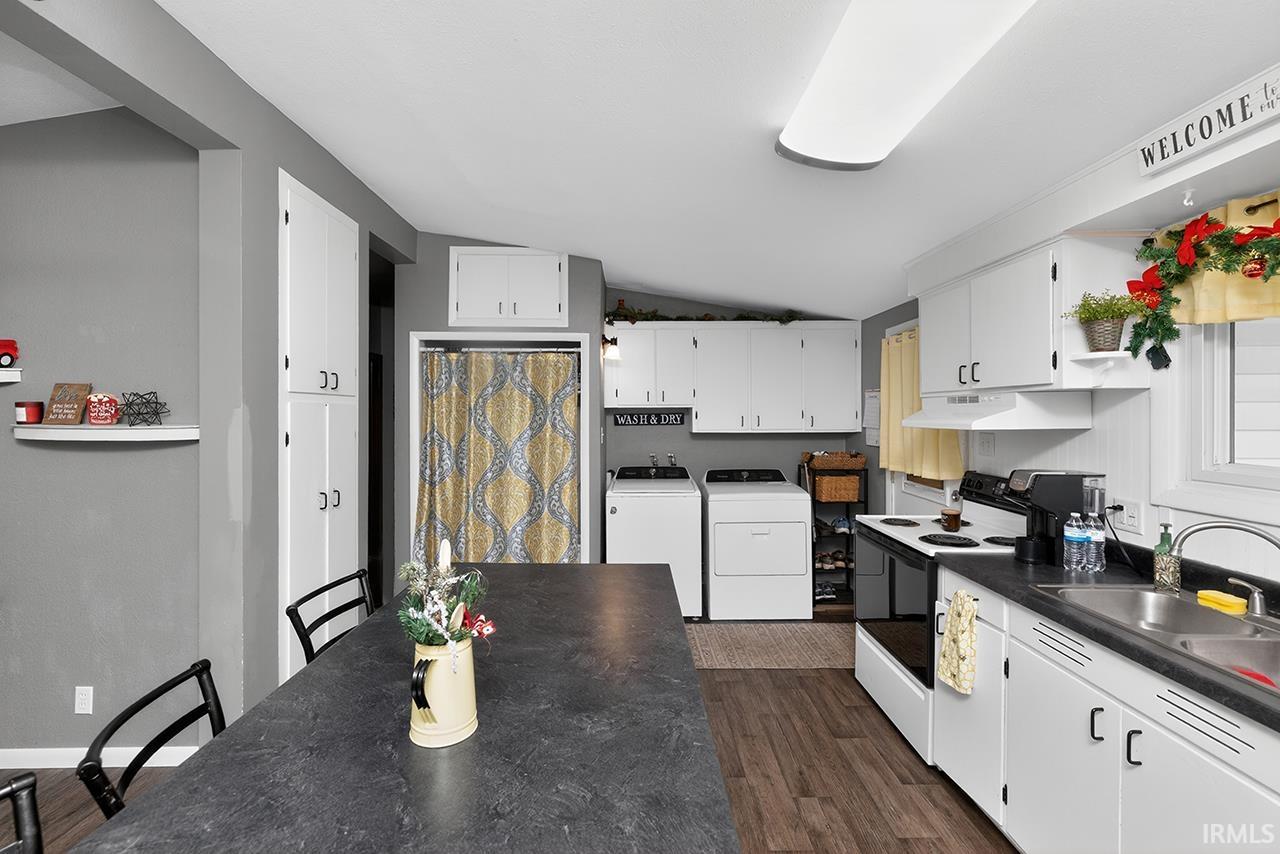 Kitchen featuring vaulted ceiling, electric range, white cabinetry, dark countertops, and dark wood-type flooring