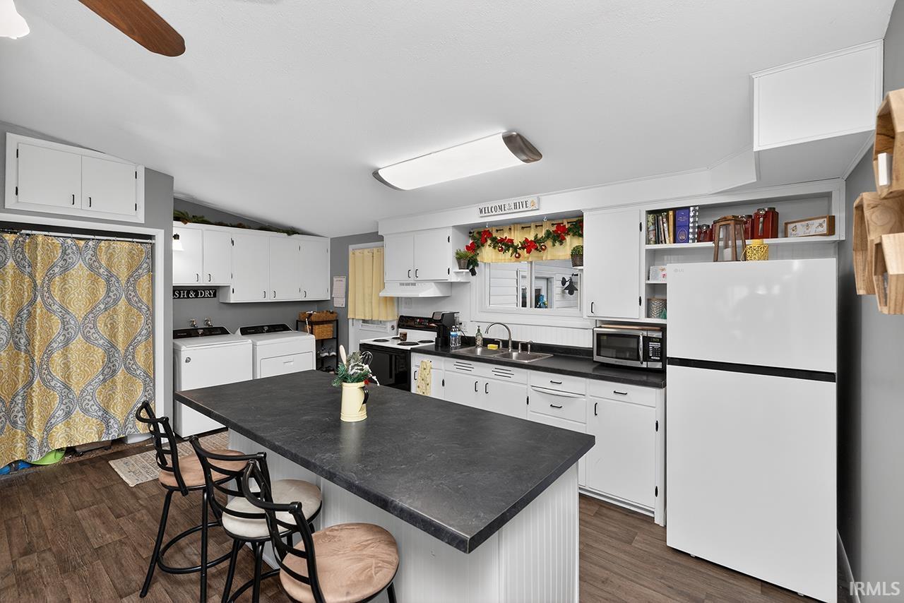 Kitchen featuring white cabinets, freestanding refrigerator, a breakfast bar area, open shelves, and vaulted ceiling
