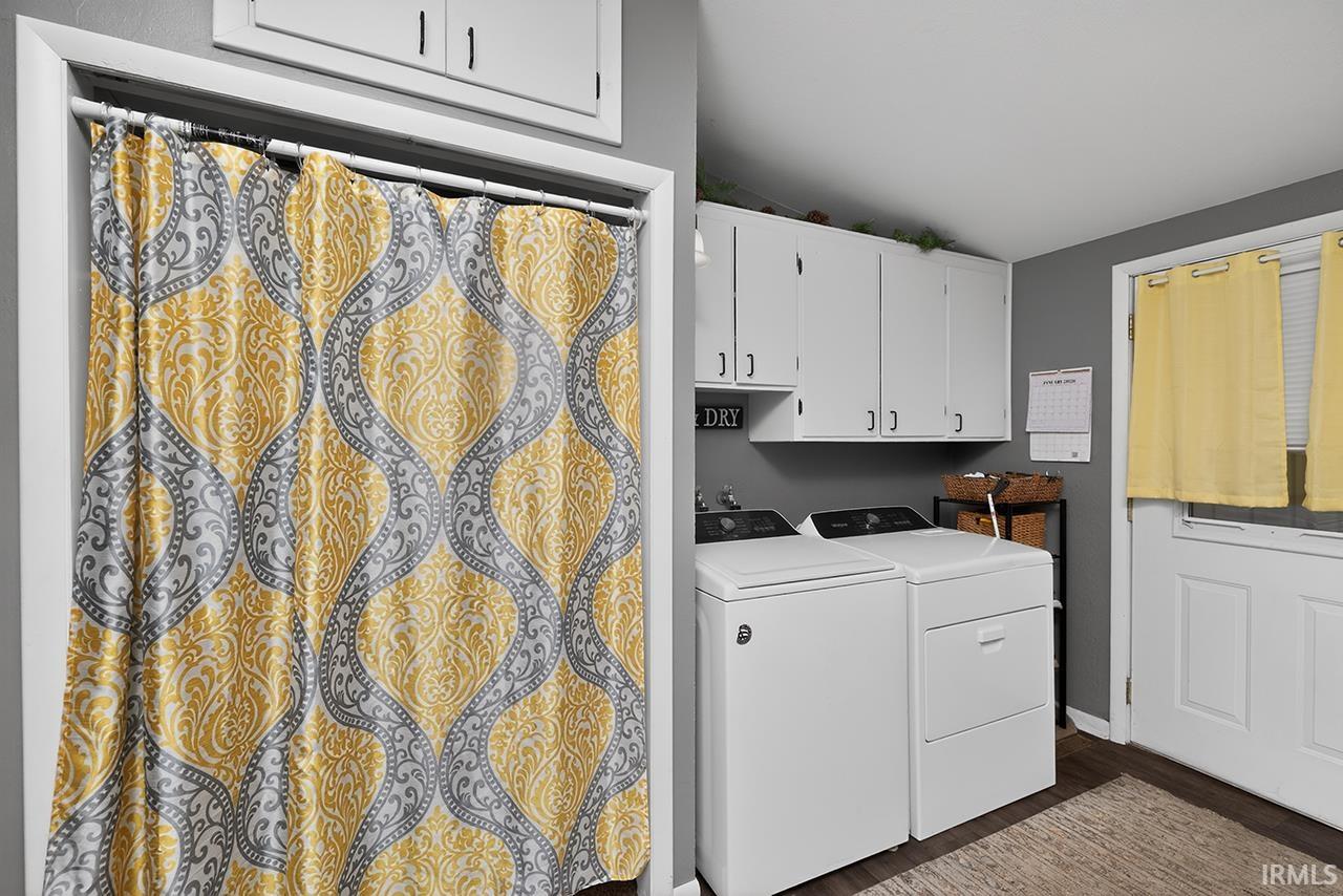 Laundry area featuring vaulted ceiling, dark wood-style floors, cabinet space, and washing machine and clothes dryer