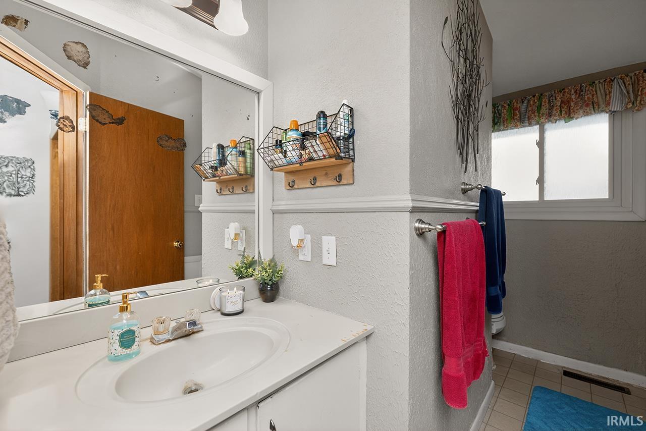 Bathroom with vanity, a textured wall, and light tile patterned flooring