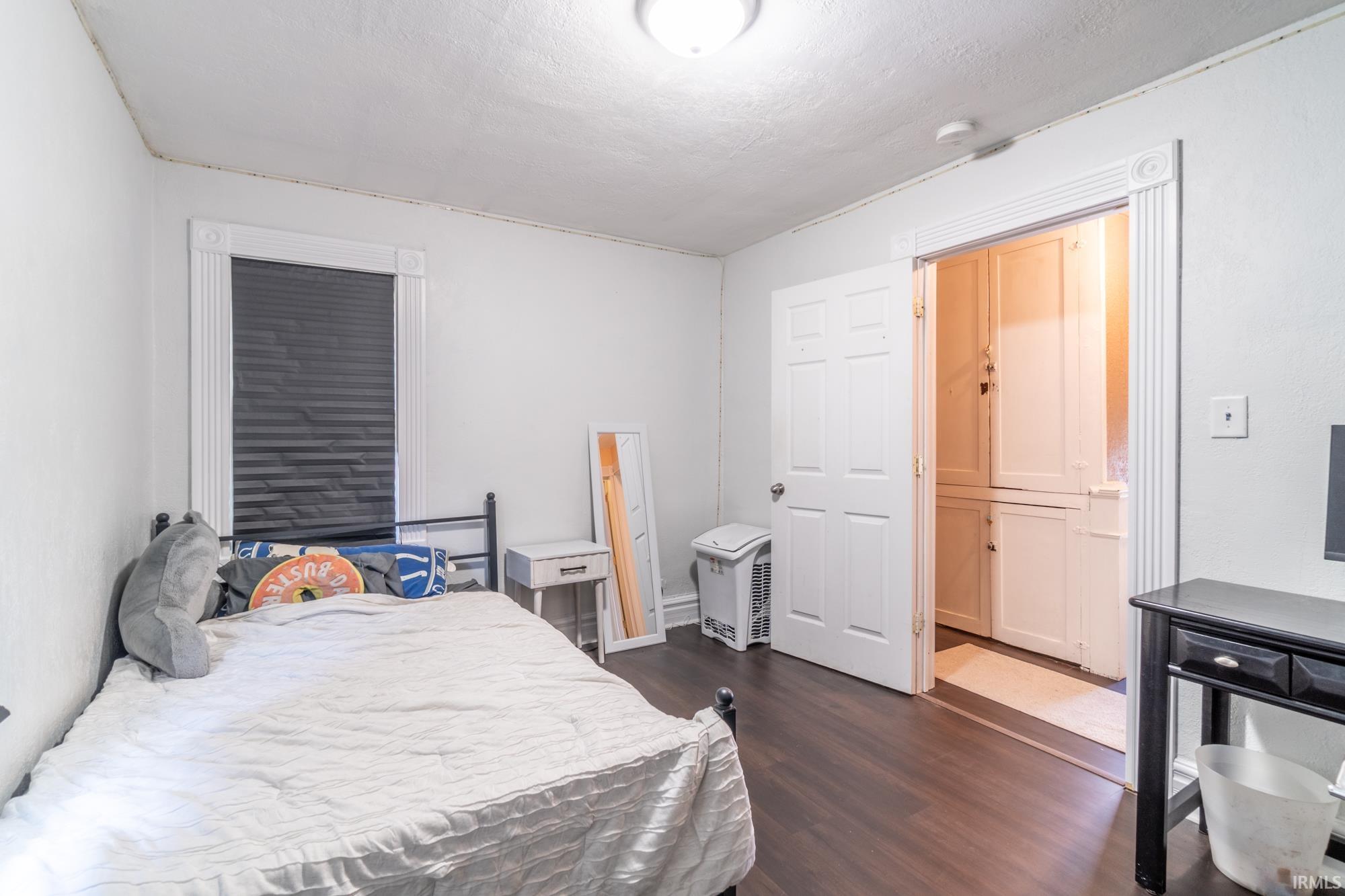 Room featuring dark wood-finish flooring, a window with horizontal blinds, and a built-in storage unit with white cabinetry