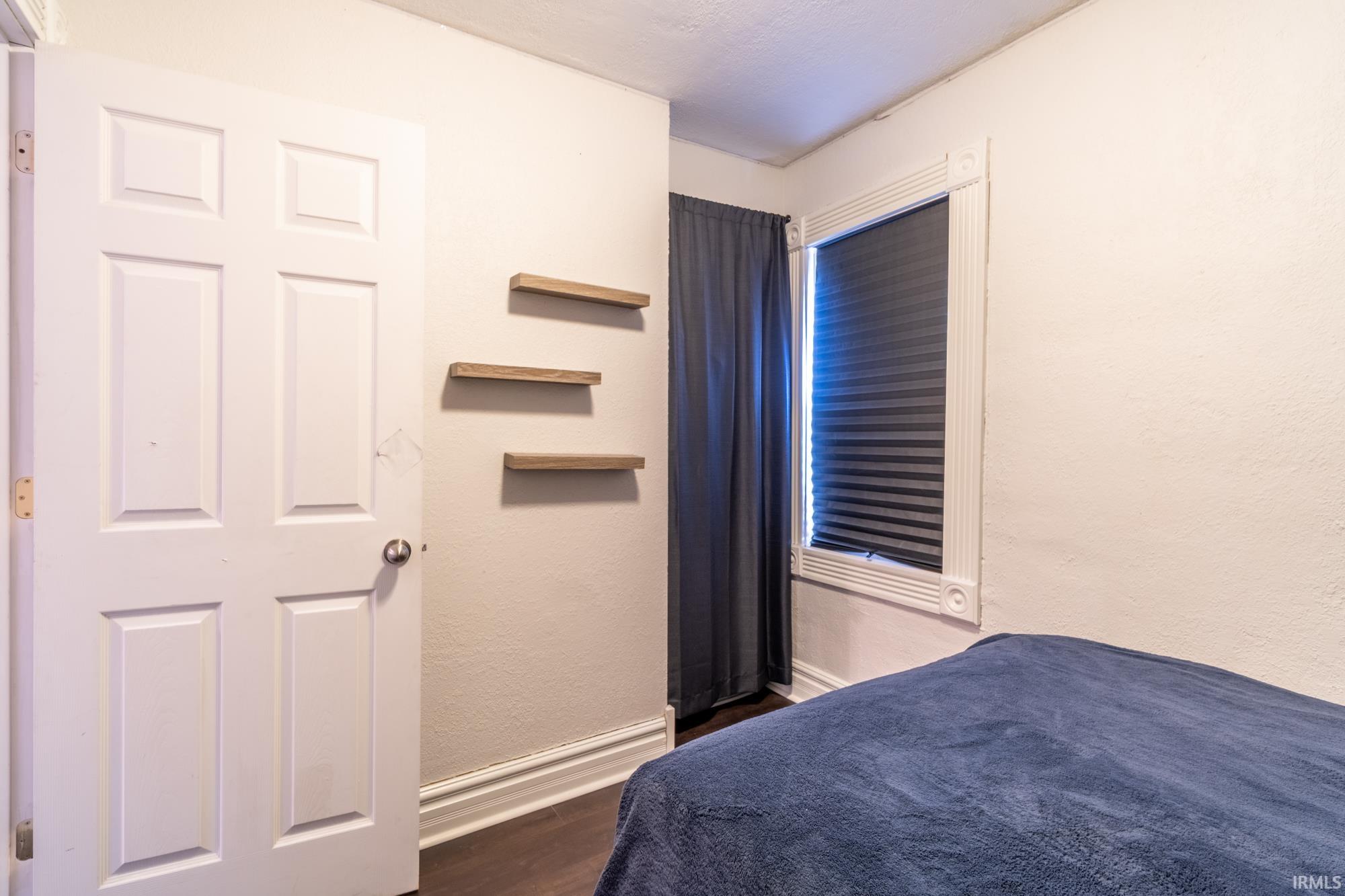 Interior room featuring a white paneled door, wood-finish flooring, and white baseboard trim