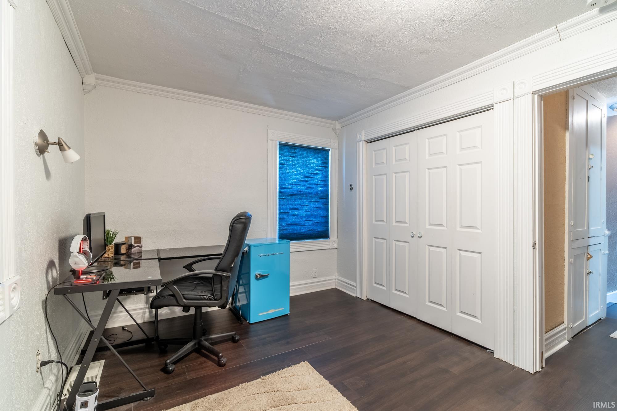 Room featuring dark wood-finish flooring, a window with blue blinds, and white bi-fold closet doors