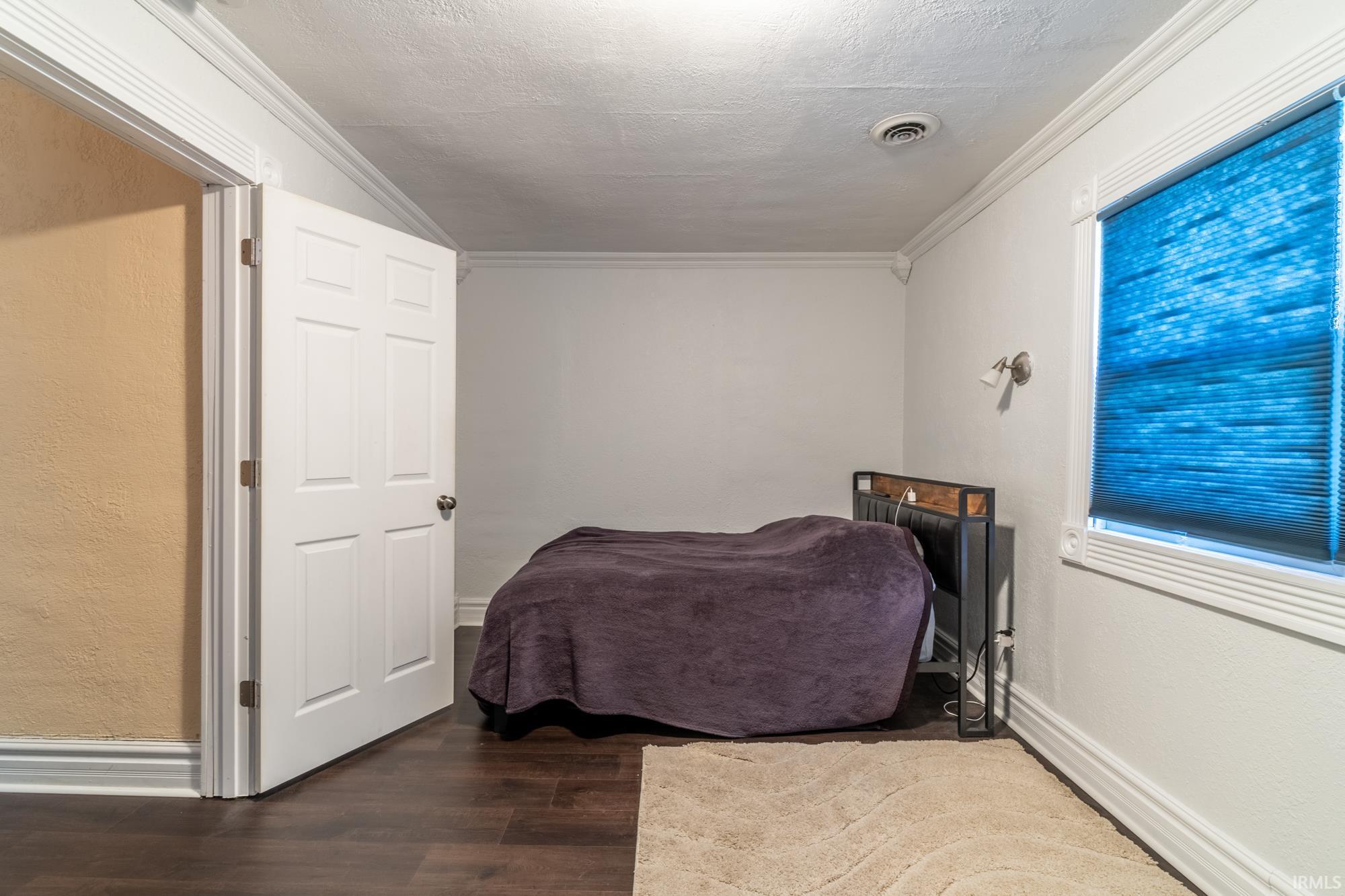 Room featuring wood-finish flooring, white trim, and crown molding