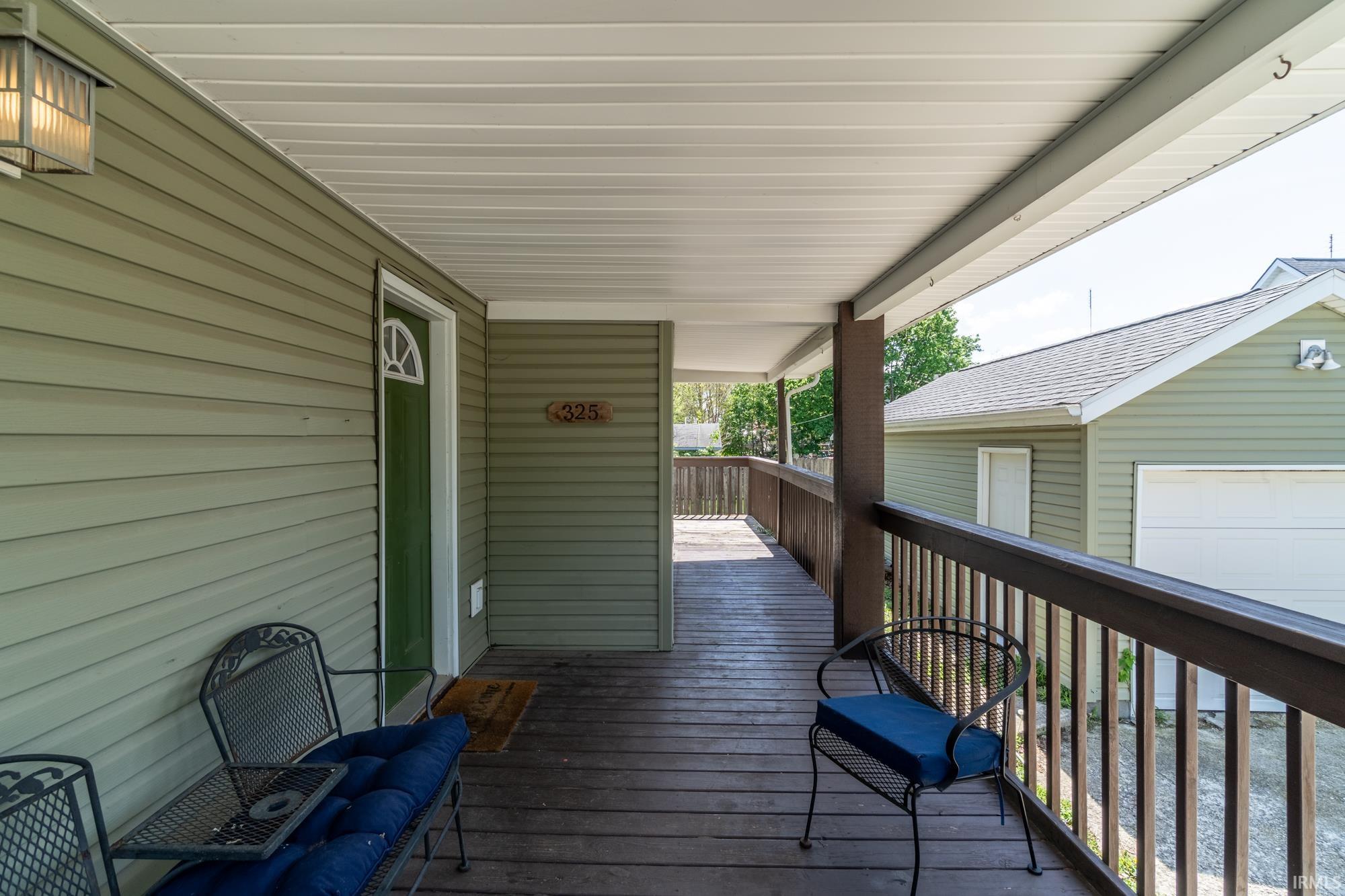 Covered porch with wood-finish flooring, wood railing, and light green horizontal siding