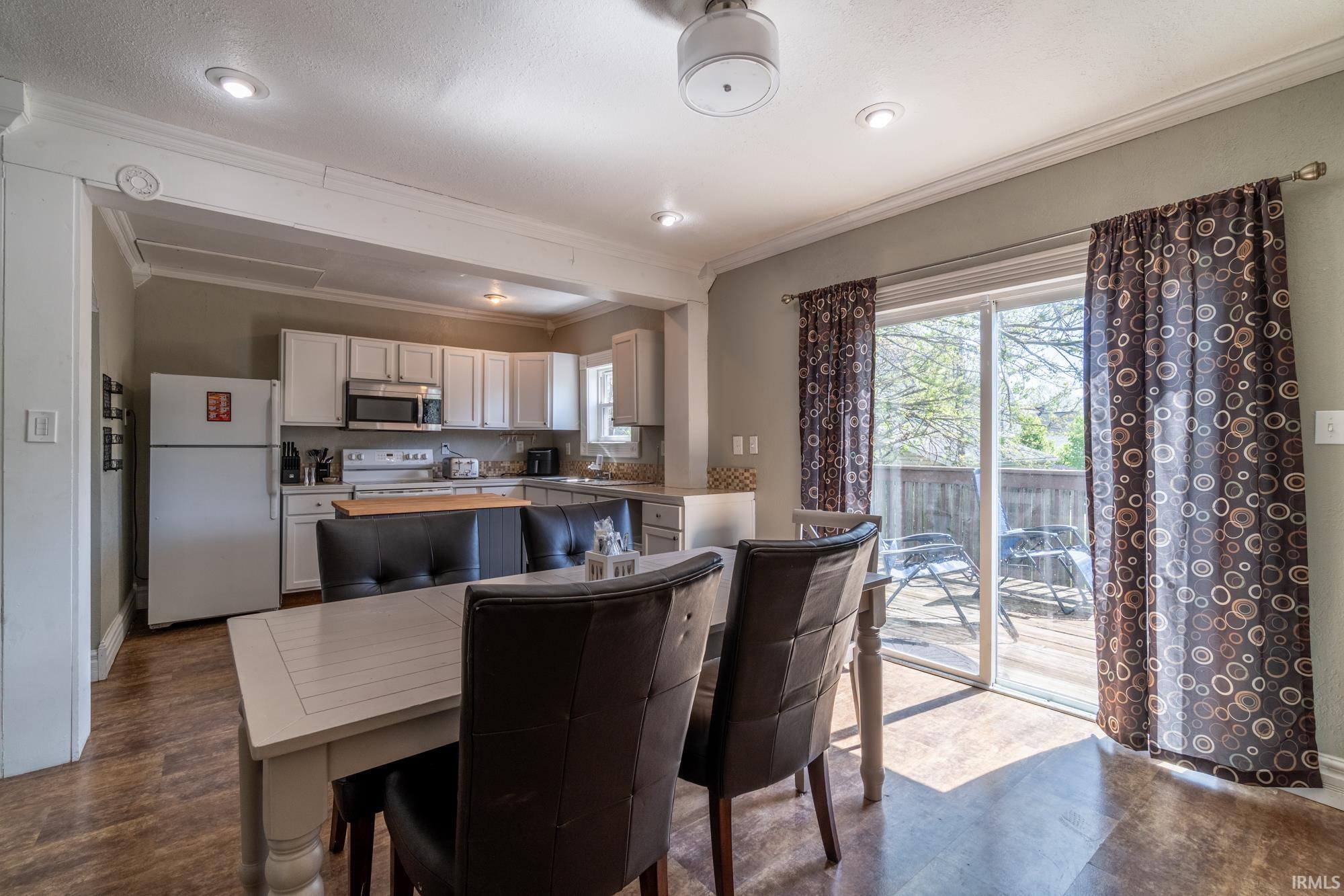 Open-concept living area featuring wood-finish flooring, a contemporary kitchen with white cabinetry and stainless steel appliances, and a sliding glass door leading to an outdoor deck