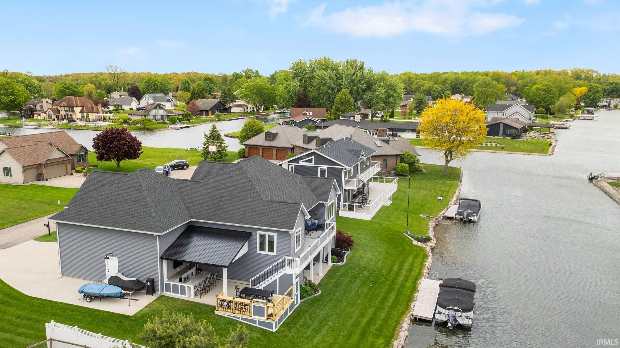 Waterfront residence featuring a covered patio, multiple upper-level balconies, expansive green lawn, private boat dock, and direct water access