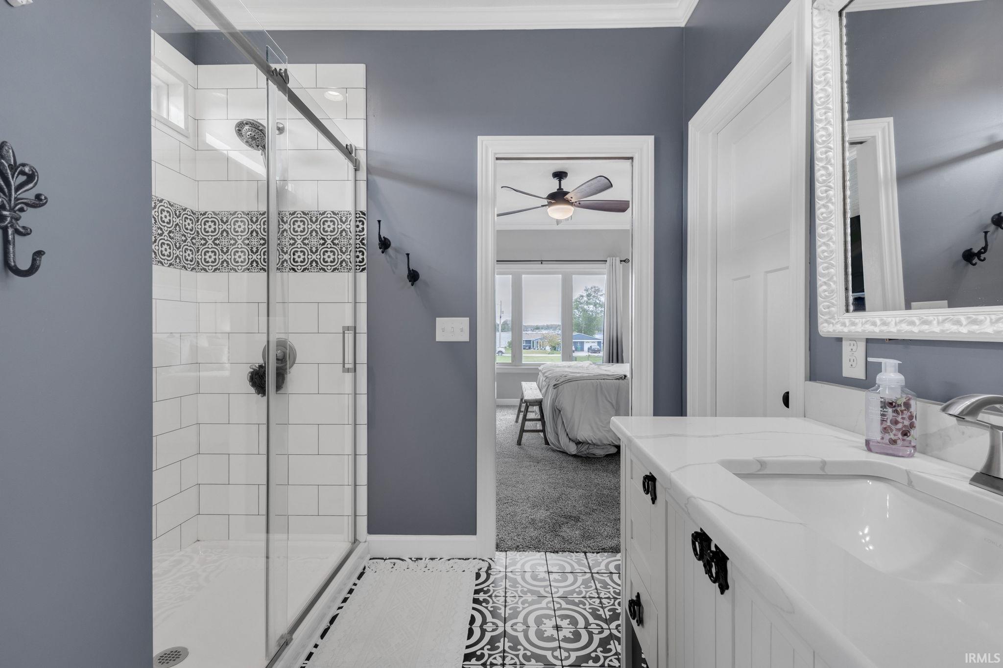 Bathroom featuring a glass-enclosed shower with subway tile and decorative accent band, a single vanity with a white countertop and undermount sink, and patterned floor tile