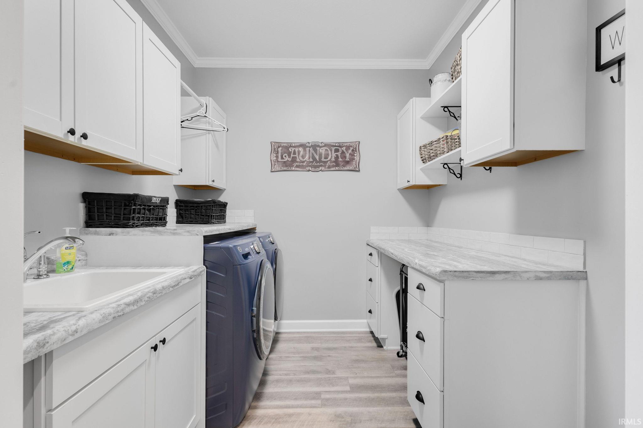 Dedicated laundry room featuring white cabinetry, light wood-finish flooring, a utility sink, and ample counter space with a light-toned finish