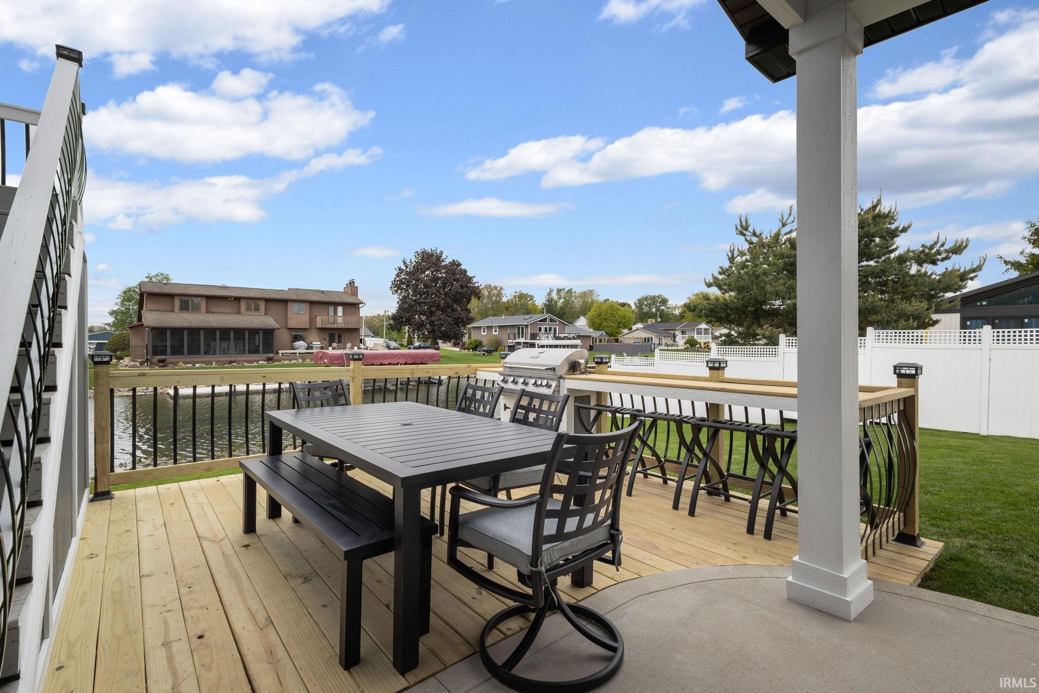 Spacious outdoor deck with a concrete patio, wood-finish flooring, and black metal railings, featuring a built-in bar area and a separate grass lawn