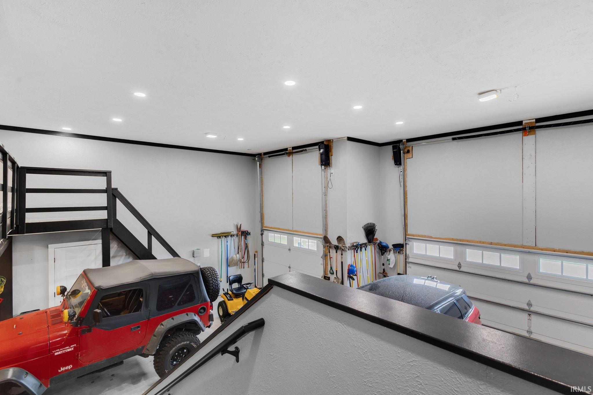 Two-story garage featuring multiple overhead doors, recessed lighting, and a loft area with a black railing system