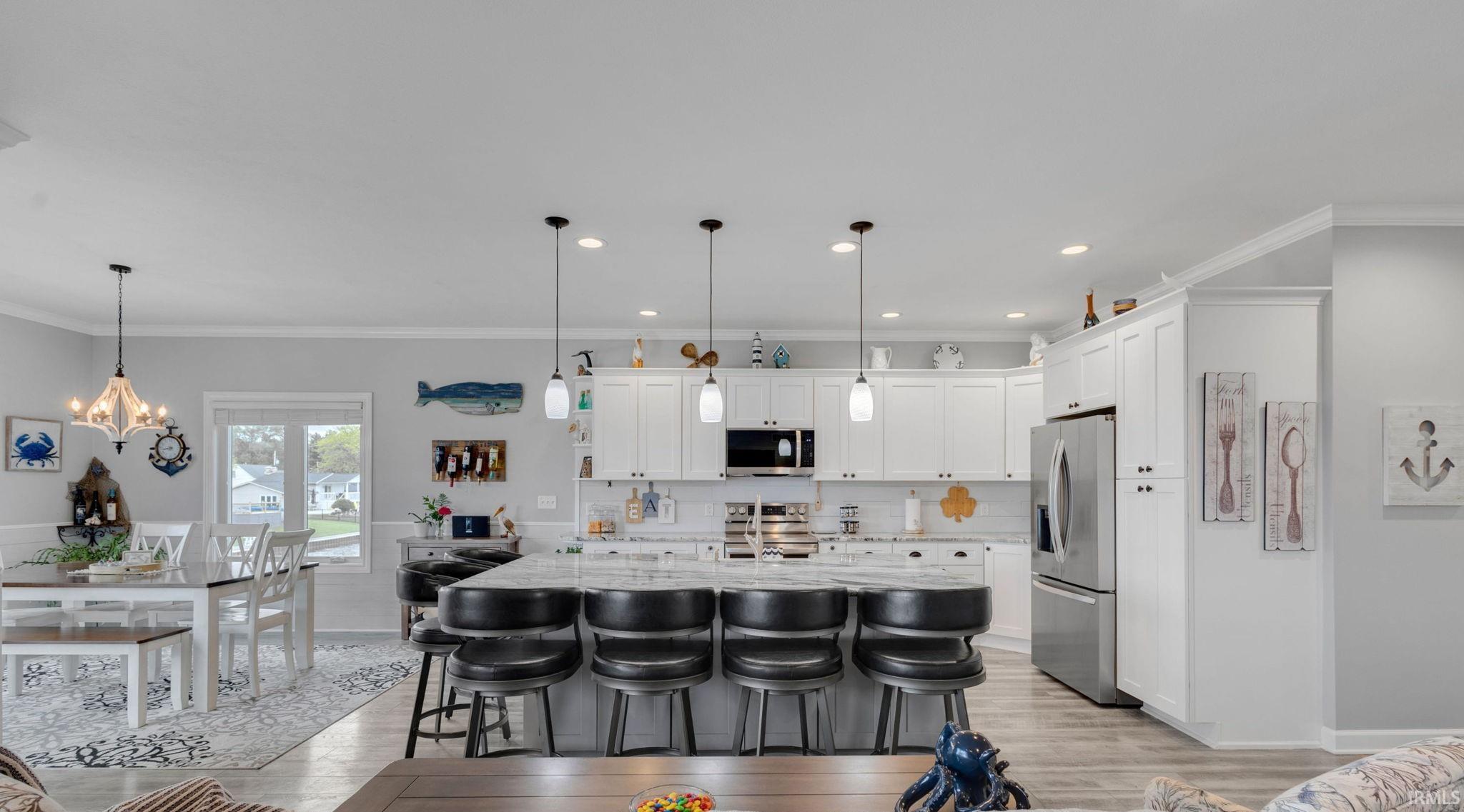 Open-concept kitchen and dining area featuring white cabinetry, stainless steel appliances, a large central island with seating, and wood-finish flooring