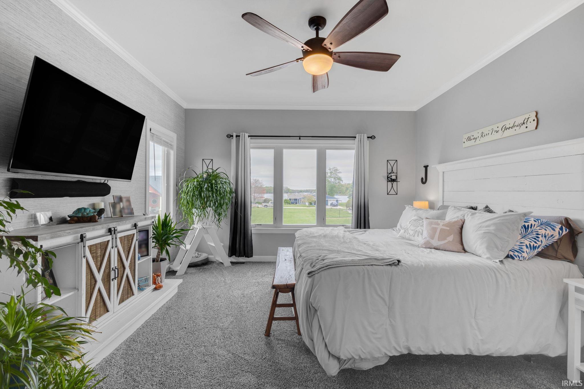 Carpeted room featuring a white shiplap headboard, wood-finish ceiling fan with integrated lighting, and multiple windows