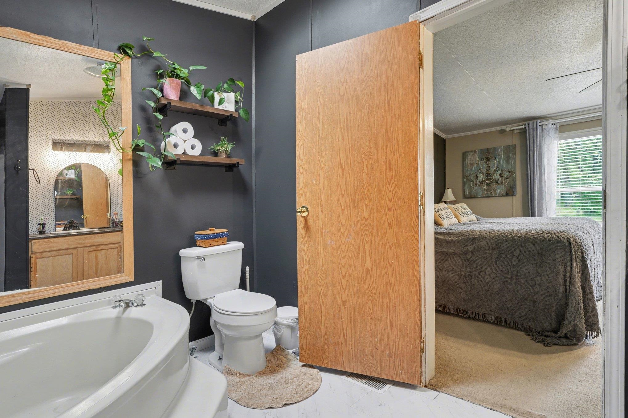 Bathroom featuring a corner soaking tub, white toilet, and dark-painted walls
