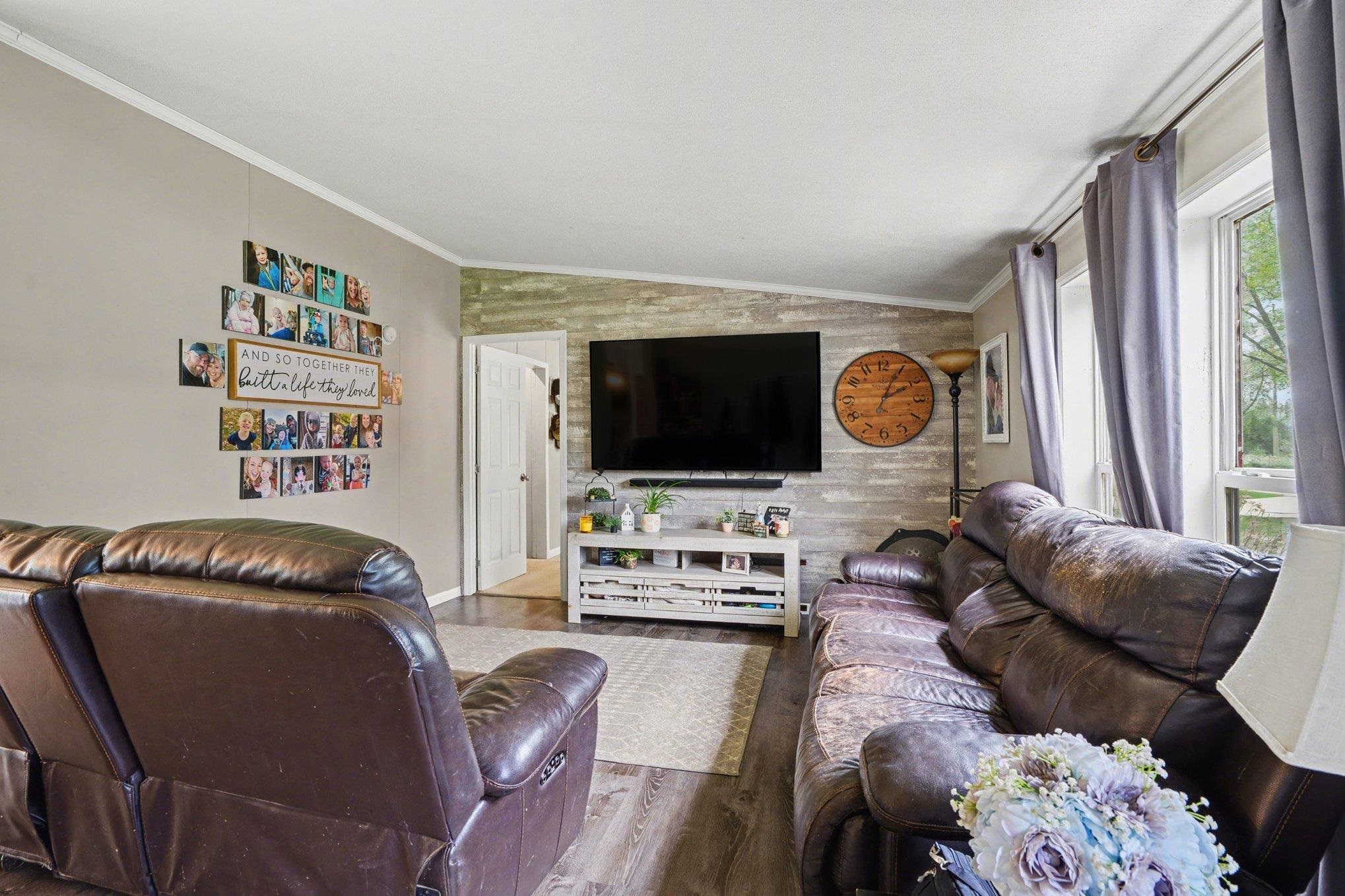 Living room featuring wood-finish flooring, a decorative accent wall, white trim, and multiple windows