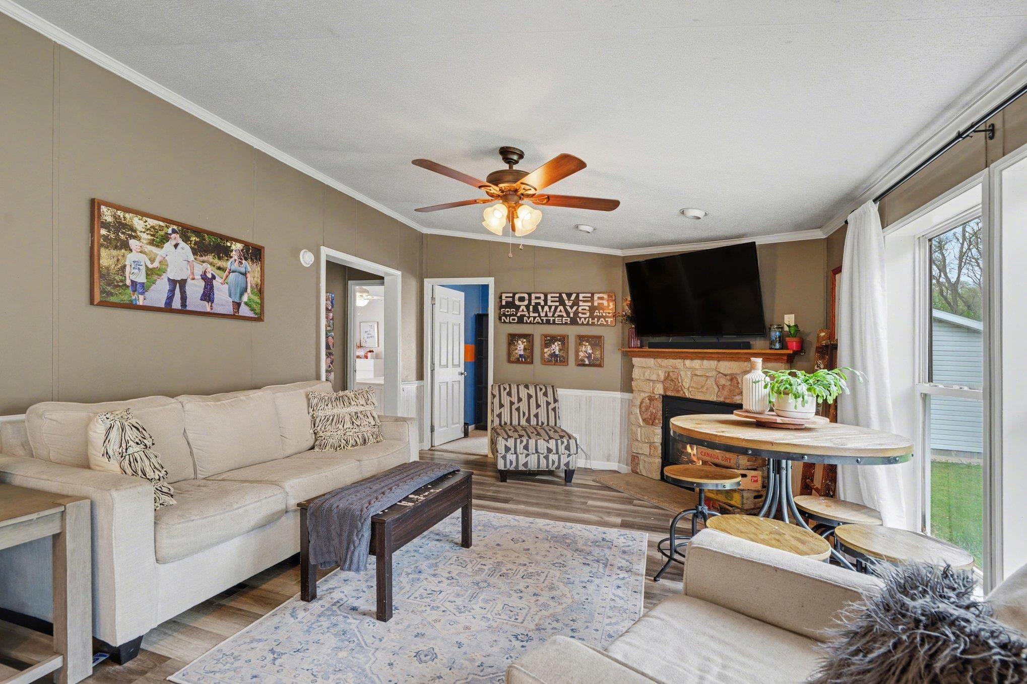 Living area featuring wood-finish flooring, a stone-surround fireplace, and a ceiling fan with integrated lighting