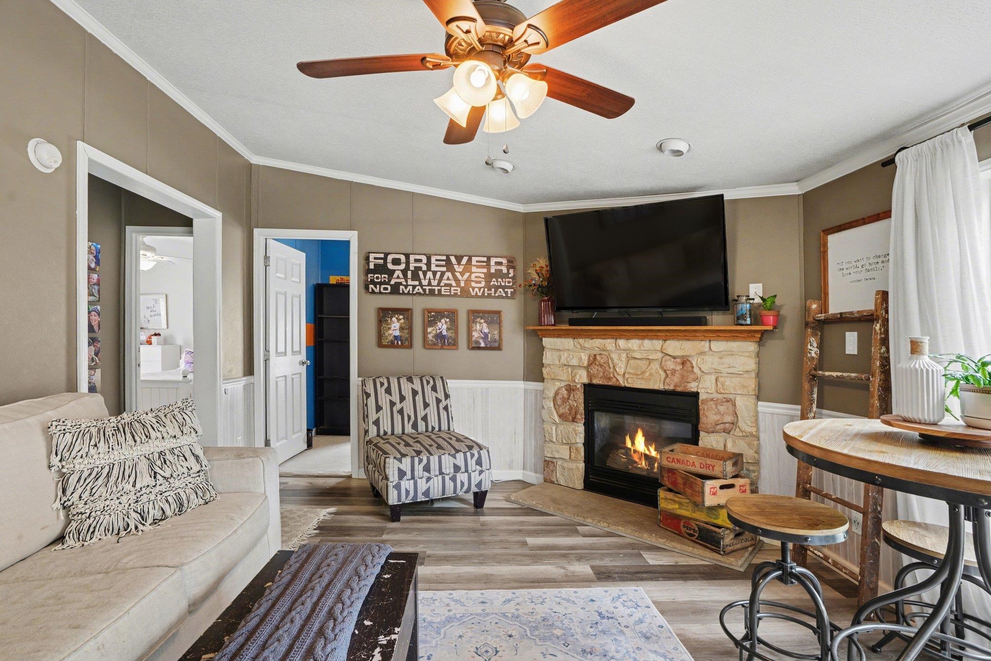 Living area featuring a stone-clad fireplace with a wood mantel, wood-finish flooring, and a ceiling fan with integrated lighting