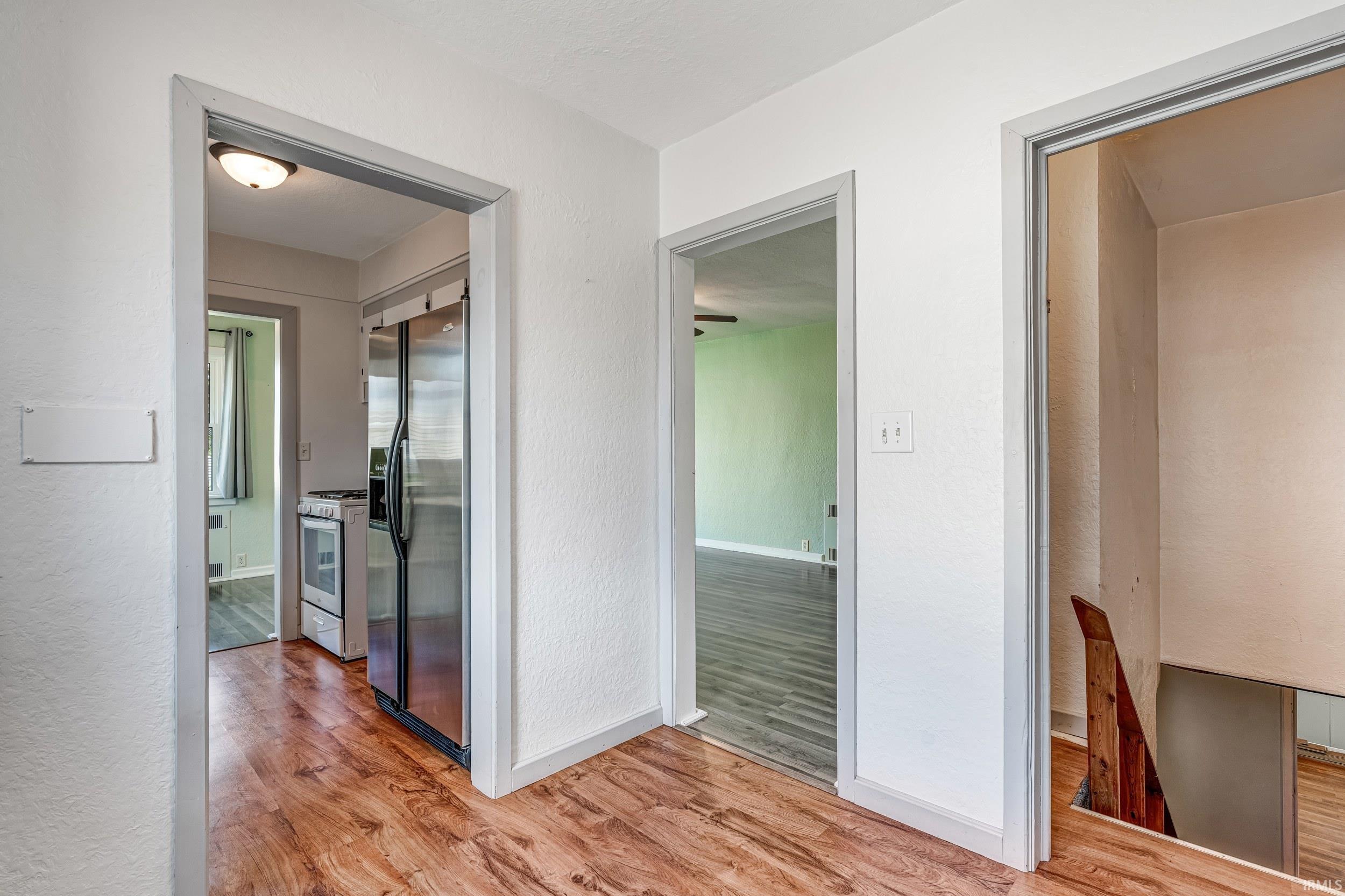 Wood-finish flooring extending through multiple doorways, featuring a stainless steel refrigerator and range, and a visible staircase