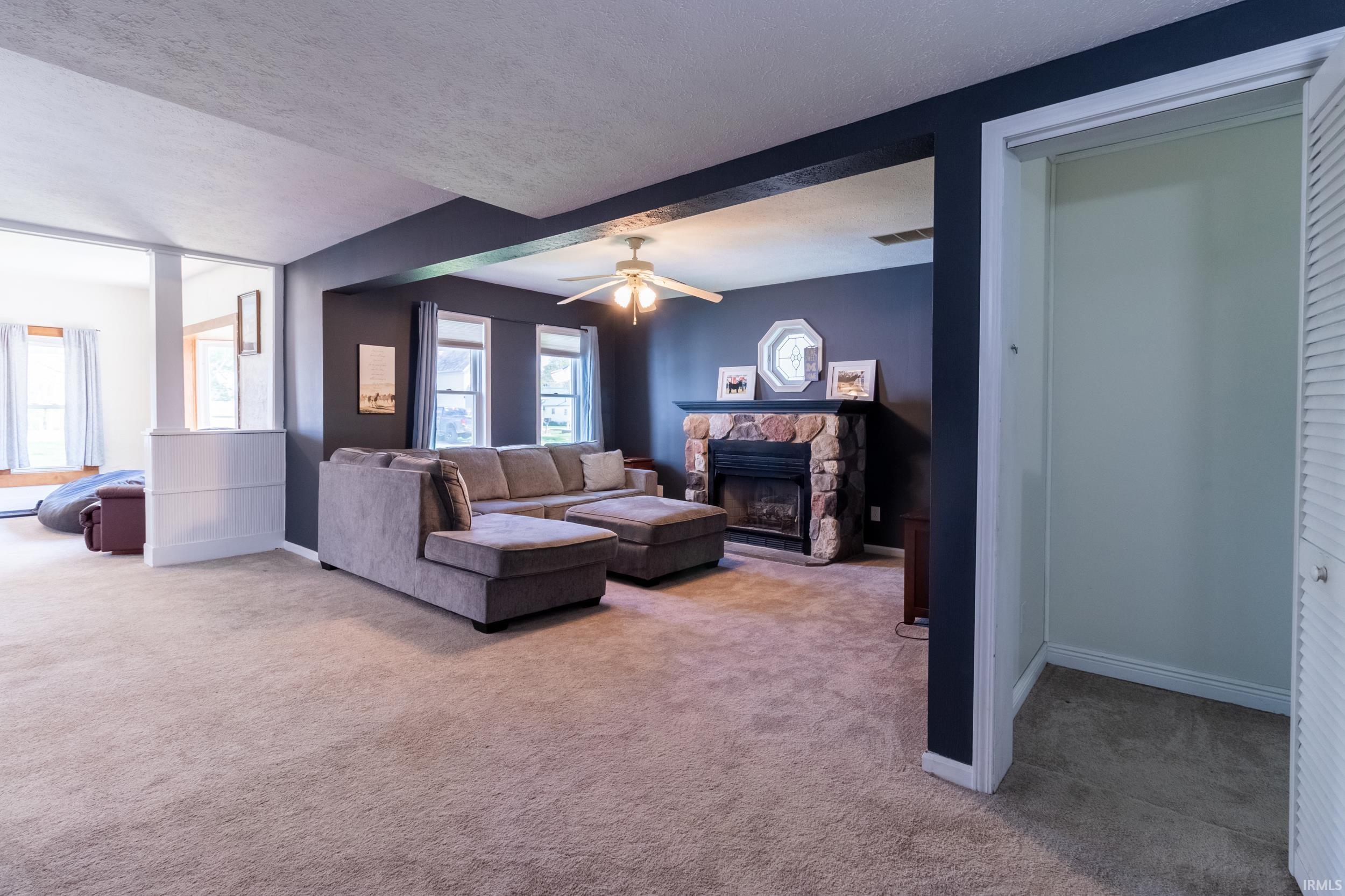 Living area featuring a stone-clad fireplace, carpet flooring, a ceiling fan, and painted walls