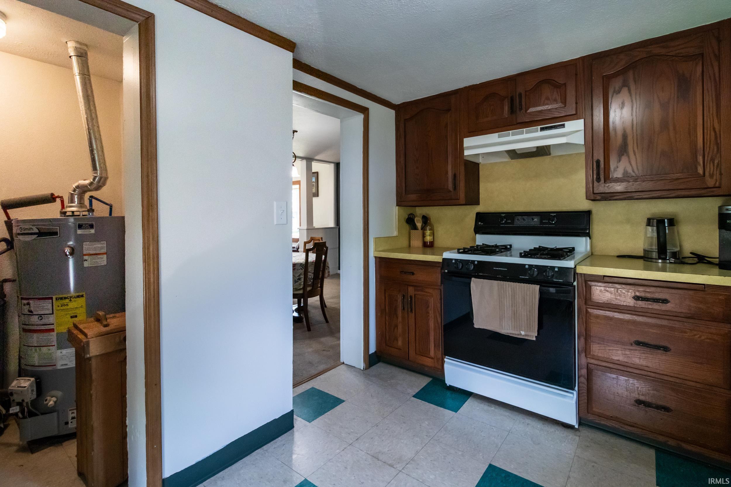 Kitchen featuring wood cabinetry, a gas range with an overhead exhaust hood, and light-toned countertops