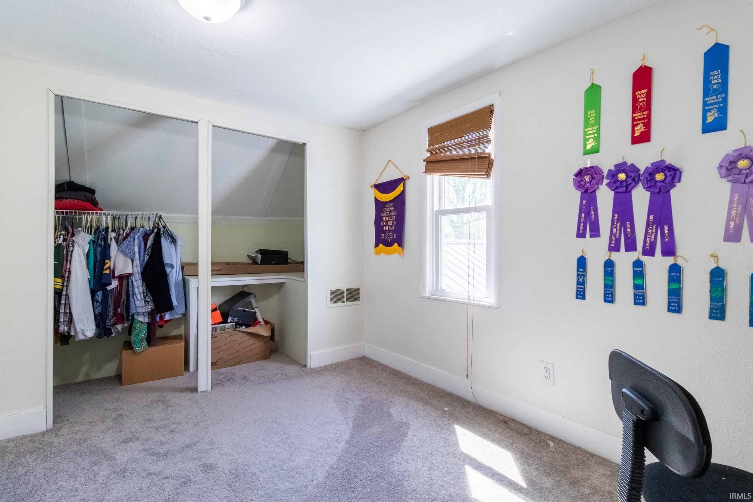 Room featuring neutral wall paint, gray carpet flooring, a window with a woven wood shade, and an angled ceiling line