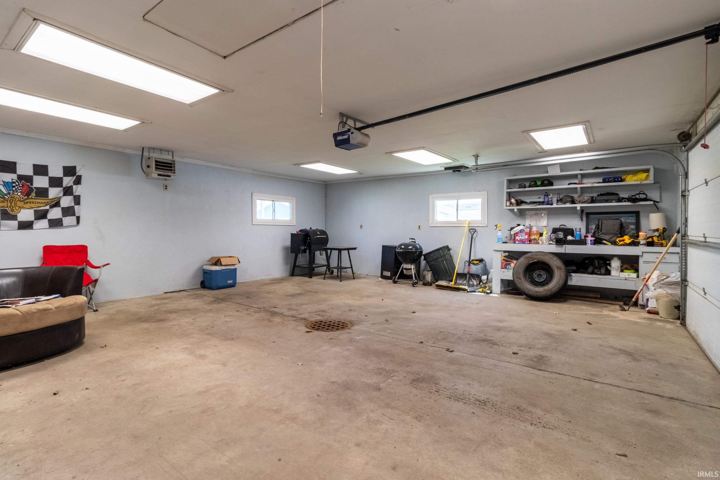 Spacious garage featuring concrete flooring, multiple windows, built-in shelving, and overhead fluorescent lighting