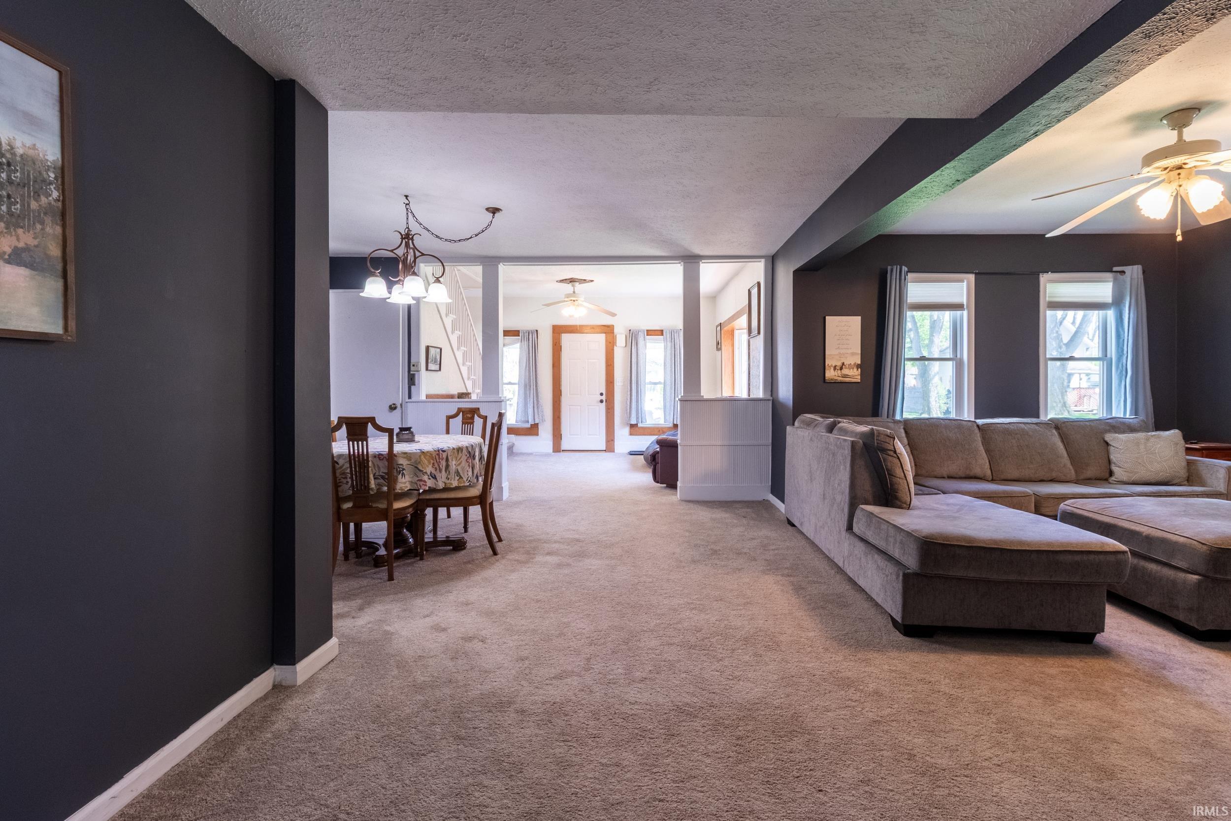 Spacious carpeted interior featuring a dining area with chandelier, a living area with dual windows, and ceiling fans