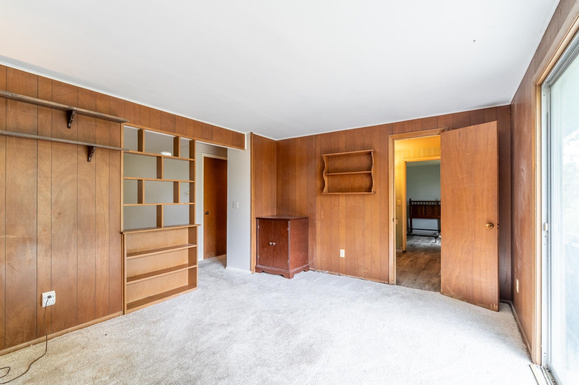 Interior room featuring wood paneling throughout, built-in shelving, light-colored carpet flooring, and a large sliding glass door