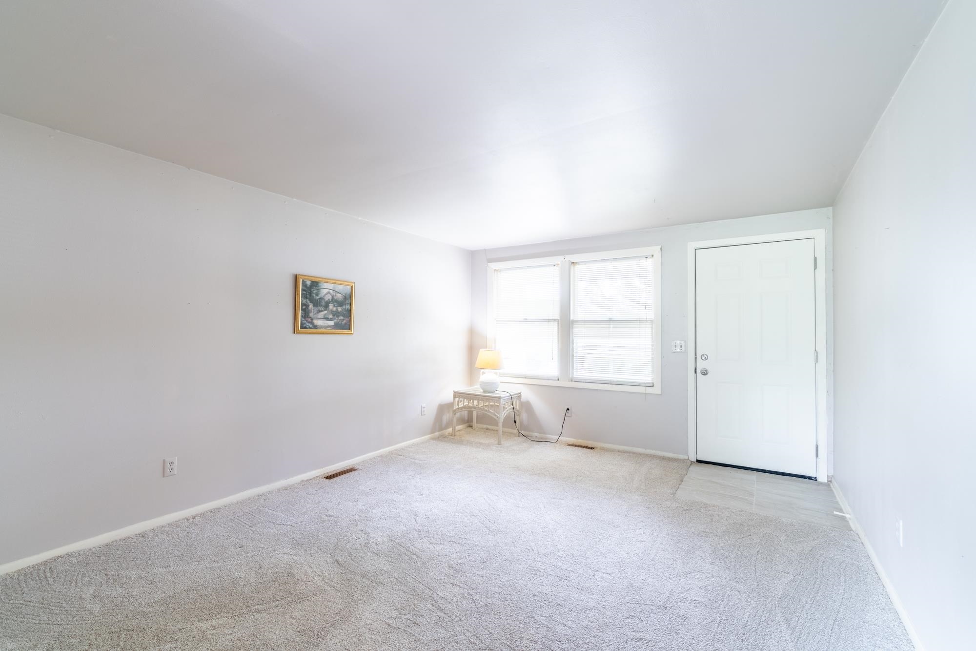 Bright room featuring light grey wall paint, two windows with white blinds, a white entry door, and light grey carpet flooring