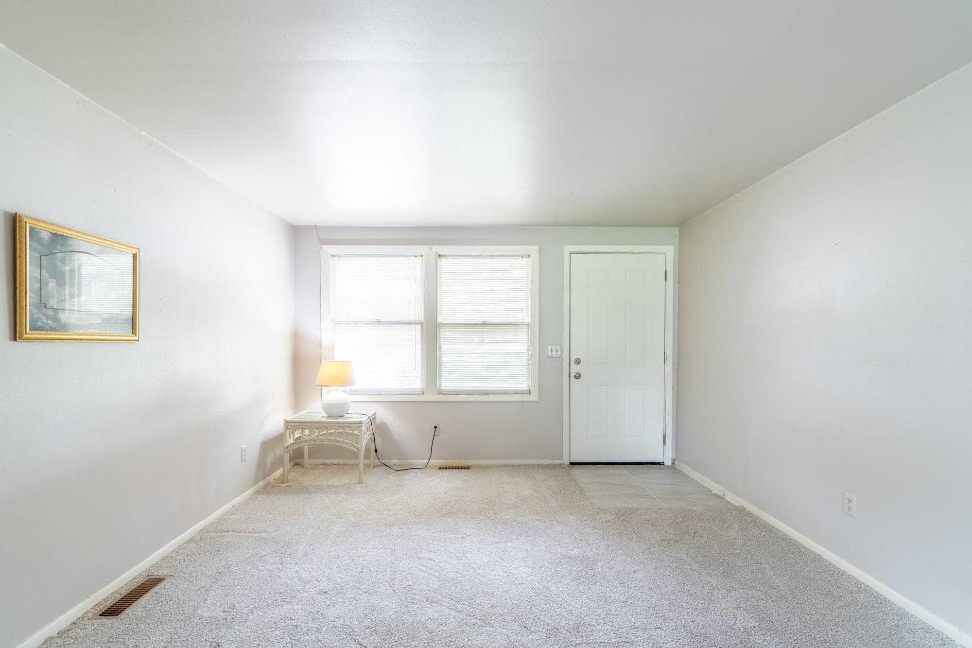 Carpeted room with a white paneled door, two windows featuring blinds, and light-toned walls