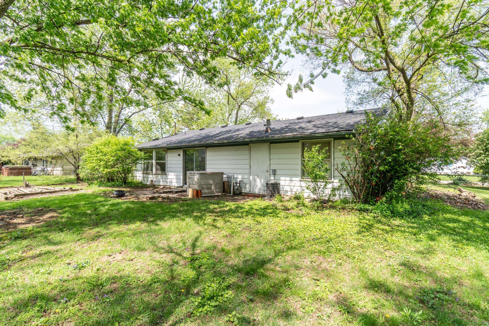 Expansive rear yard featuring green lawn, mature trees providing natural canopy, and a single-story residence with white siding