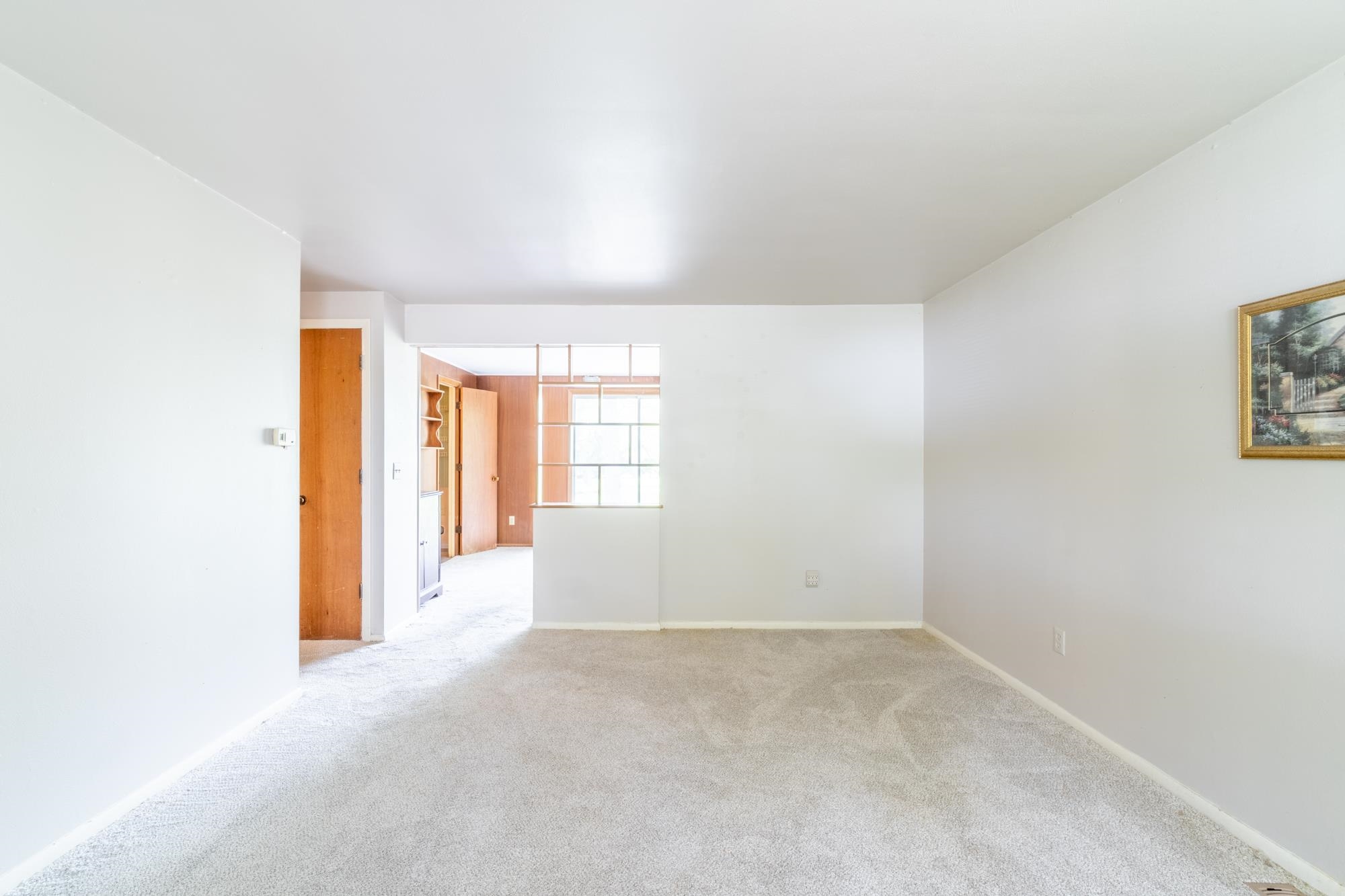 Carpeted living area with light-colored walls and a partial dividing wall featuring a window opening