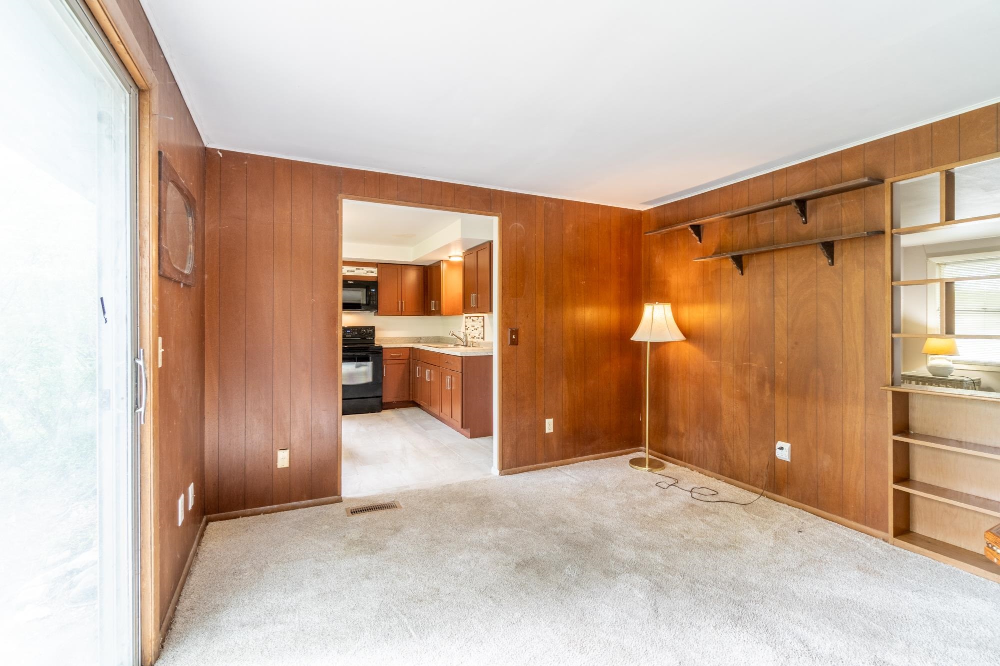Living area featuring wood paneling, light-colored carpeting, built-in shelving, and a sliding glass door