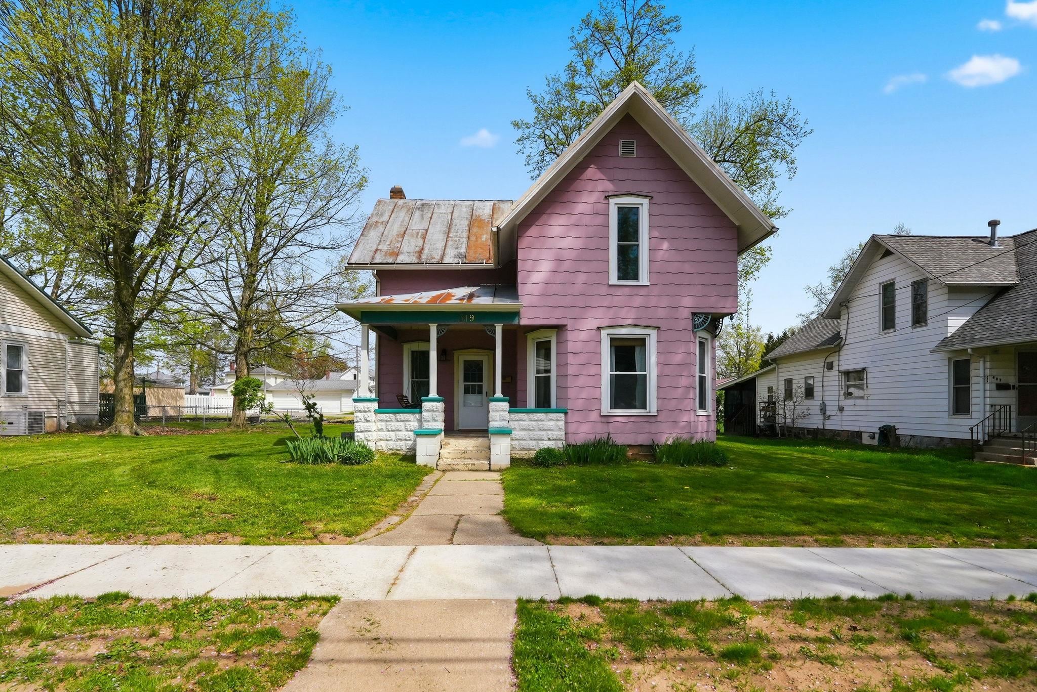 Two-story residence featuring a front porch with decorative columns, a concrete walkway, and an expansive front lawn