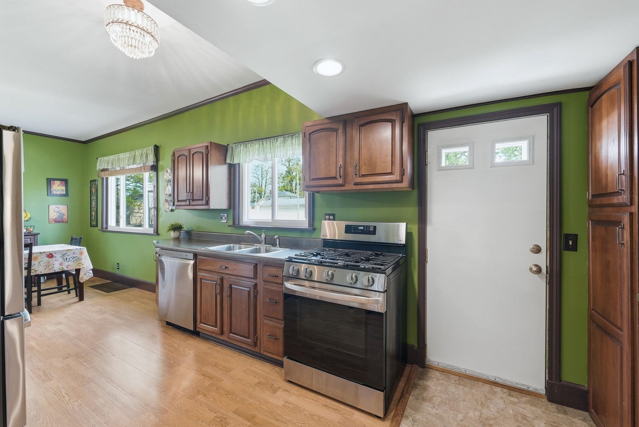 Kitchen featuring wood-finish flooring, stainless steel appliances, dark wood cabinetry, two windows, and a white exterior door with window inserts