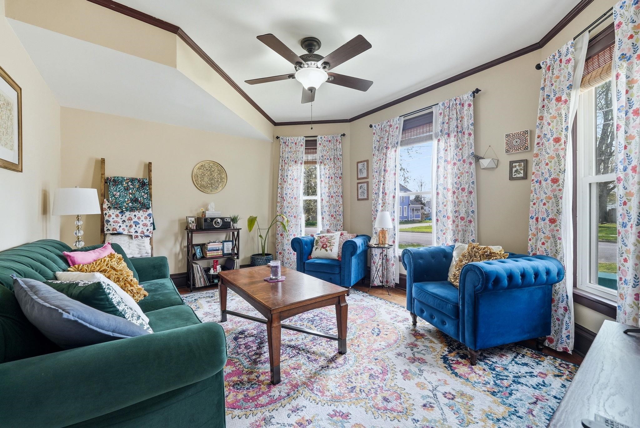 Living area featuring wood-finish flooring, a tray ceiling with a ceiling fan, and multiple windows providing natural light