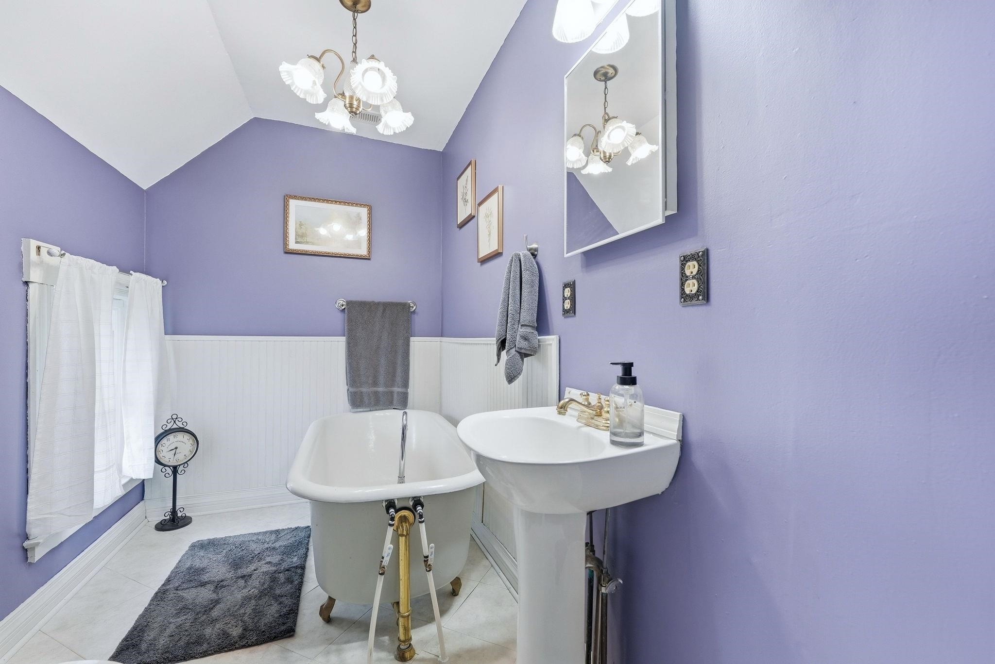 Bathroom featuring a clawfoot tub with brass hardware, pedestal sink, wall-mounted mirror, and beadboard wainscoting