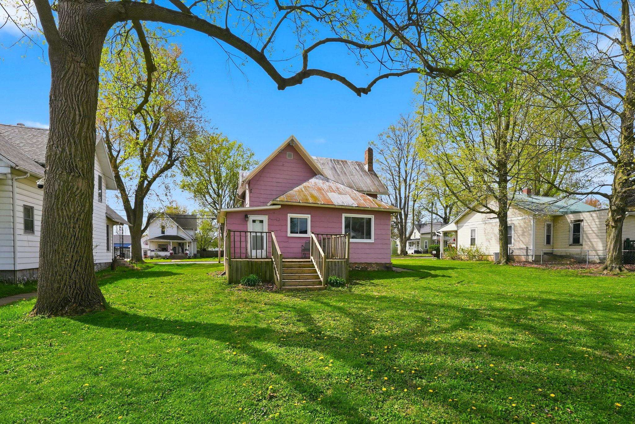 Pink exterior home with a partial porch and steps, featuring a metal roof and a prominent chimney