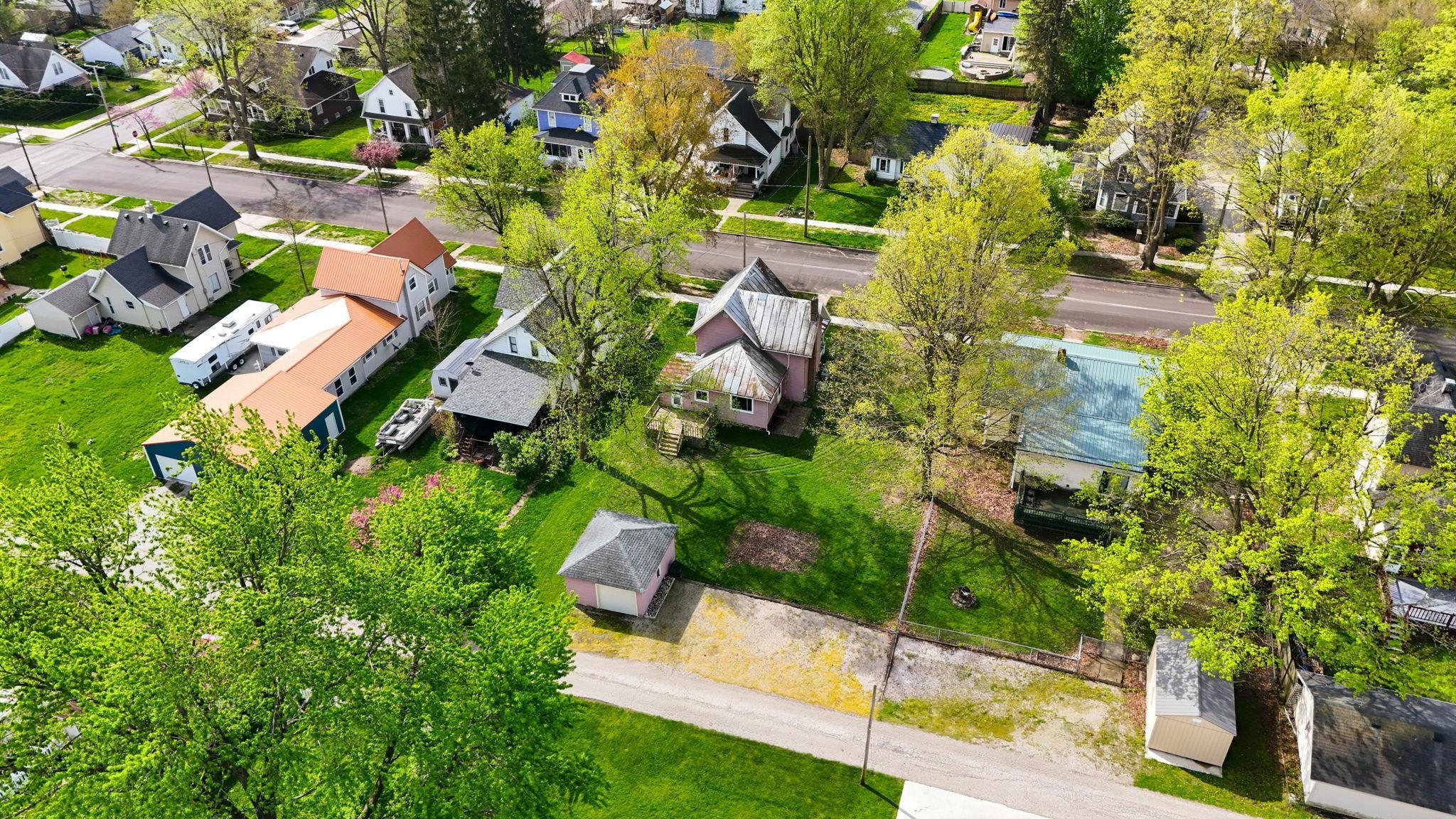 Aerial perspective showcasing a residential street with multiple properties, mature trees, and a clear sky