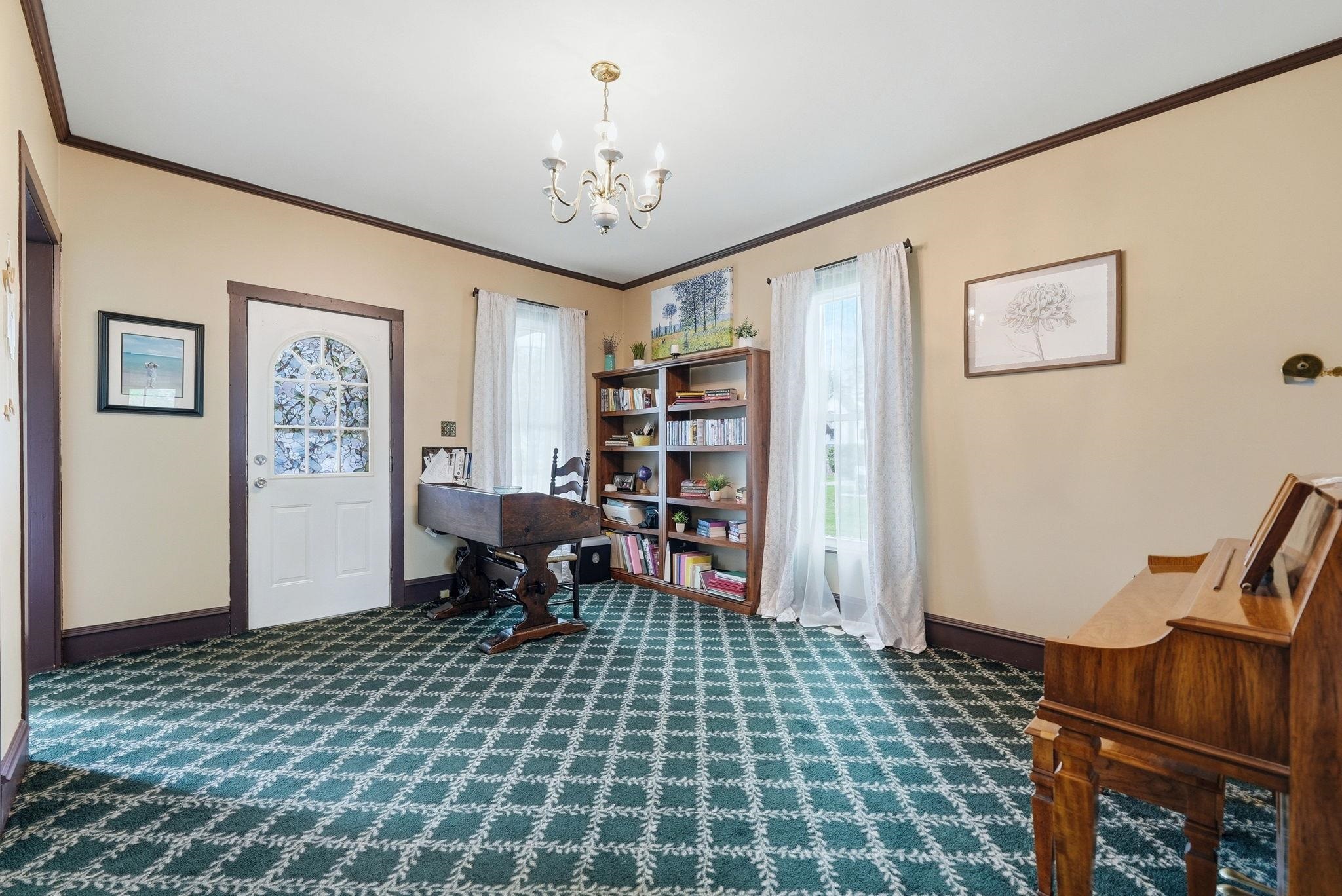 Spacious room featuring patterned green carpeting, a white paneled door with an arched glass insert, and a traditional chandelier