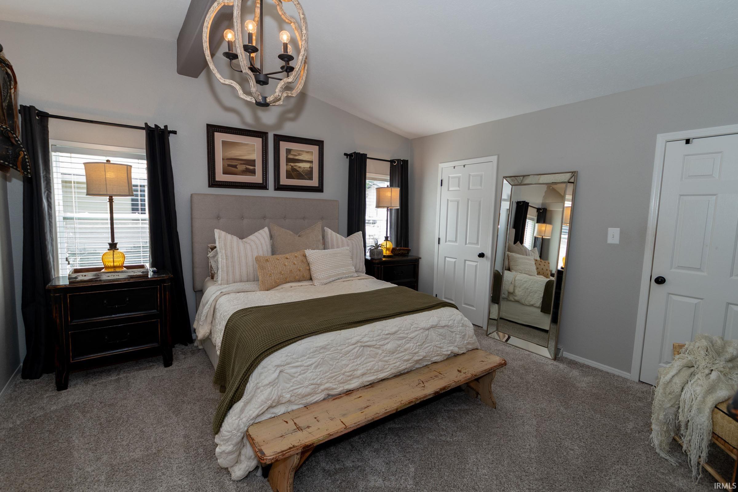 Bedroom featuring a vaulted ceiling with a decorative chandelier, a light gray upholstered headboard, and dual windows with blinds
