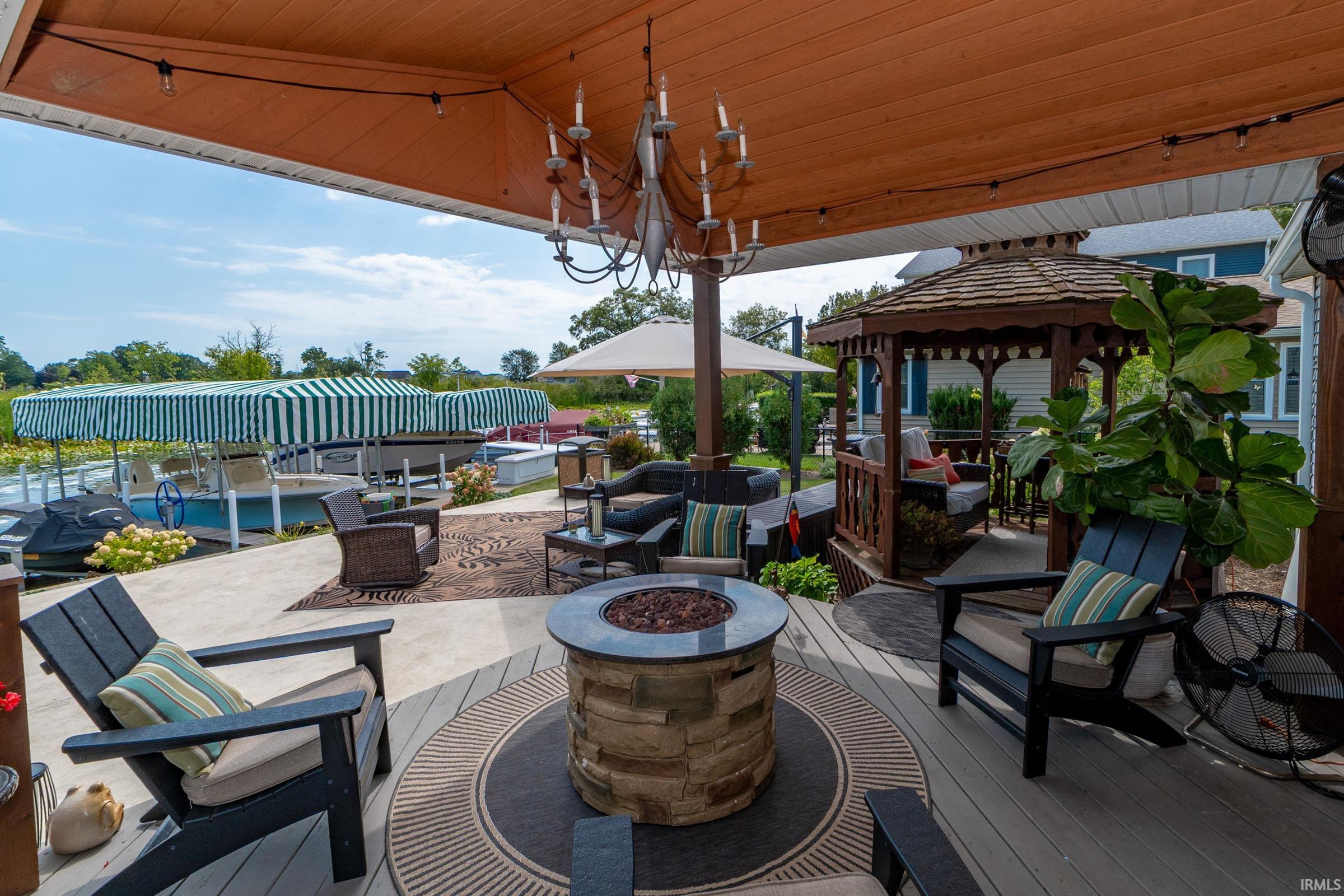 Expansive outdoor living area featuring a covered deck, stone-clad fire pit, and a separate wooden gazebo