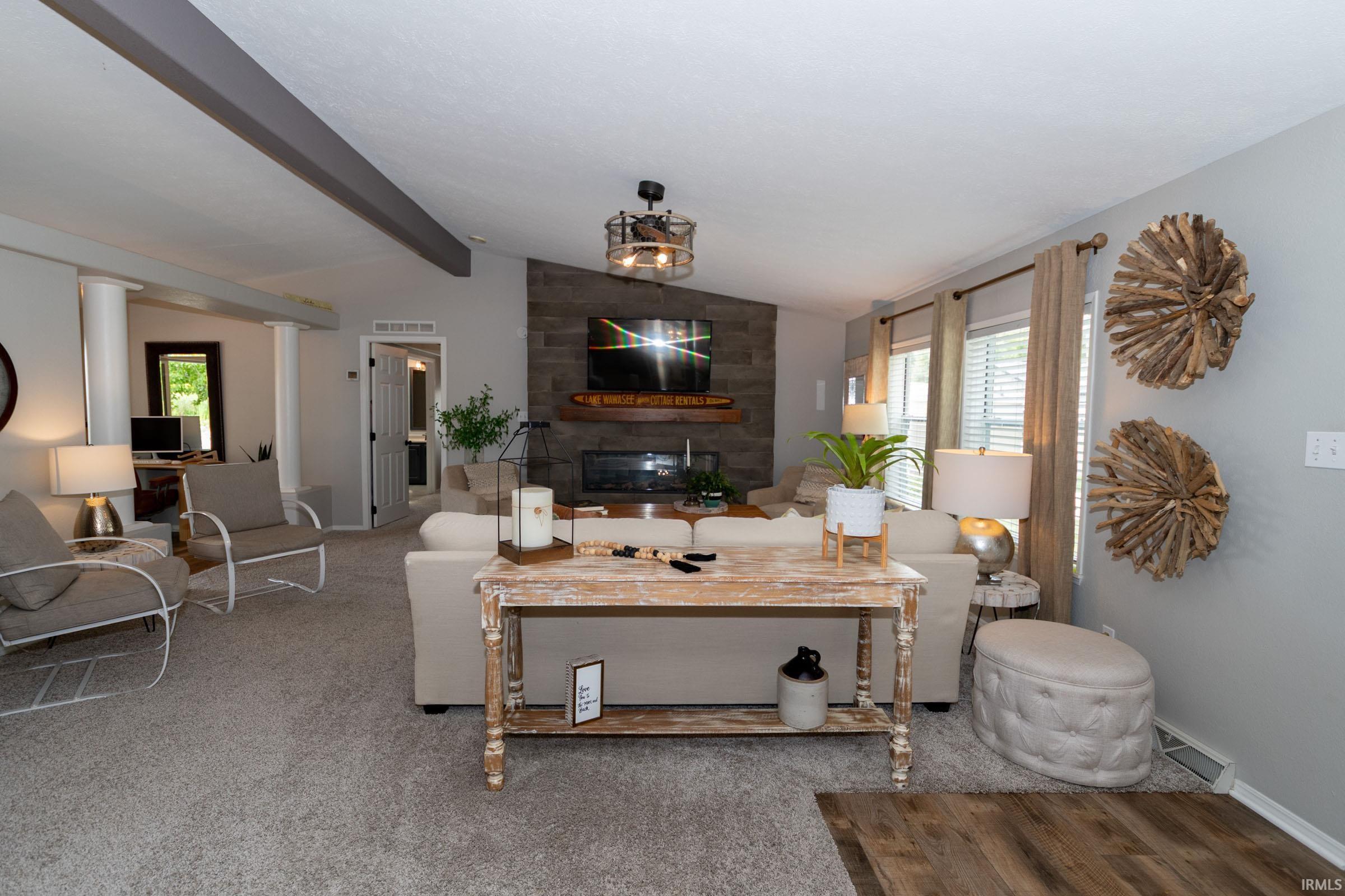 Spacious living area featuring a vaulted ceiling with exposed beams, an accent wall with a built-in fireplace, and expansive windows
