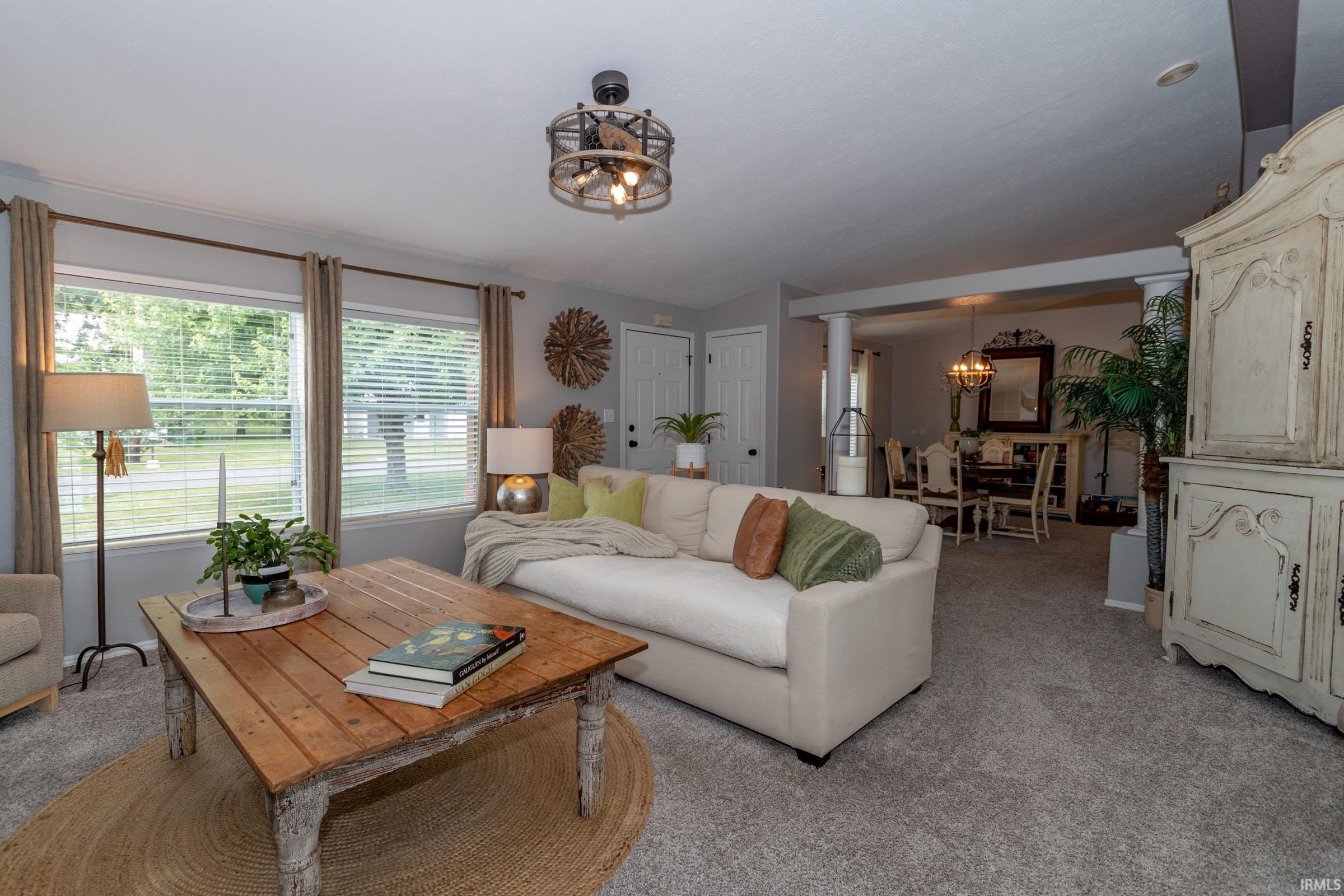 Spacious living area featuring soft grey carpeting and multiple windows with blinds