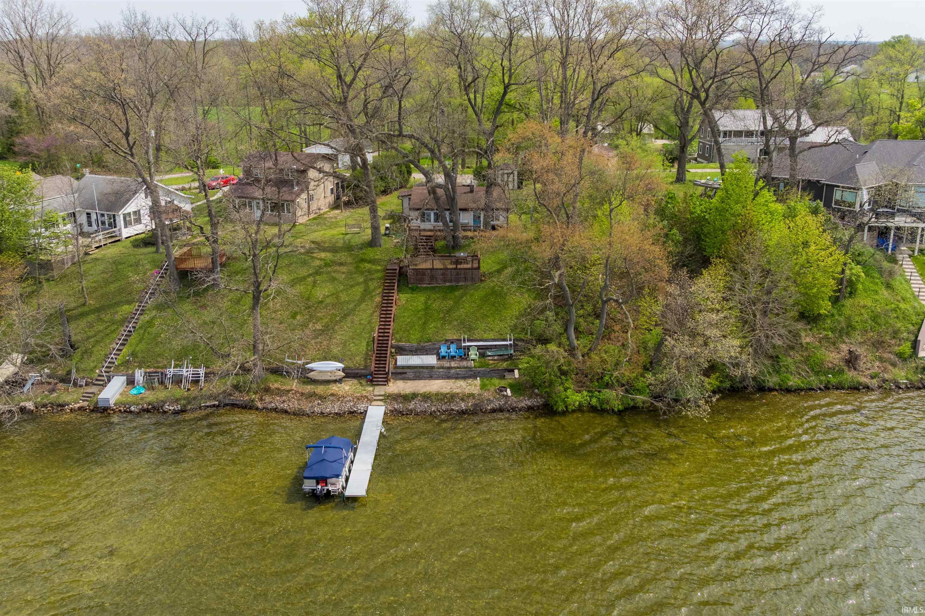 Lakeside property featuring a boat dock, tiered wooden stairway access to the water, and a sloped, tree-lined lawn