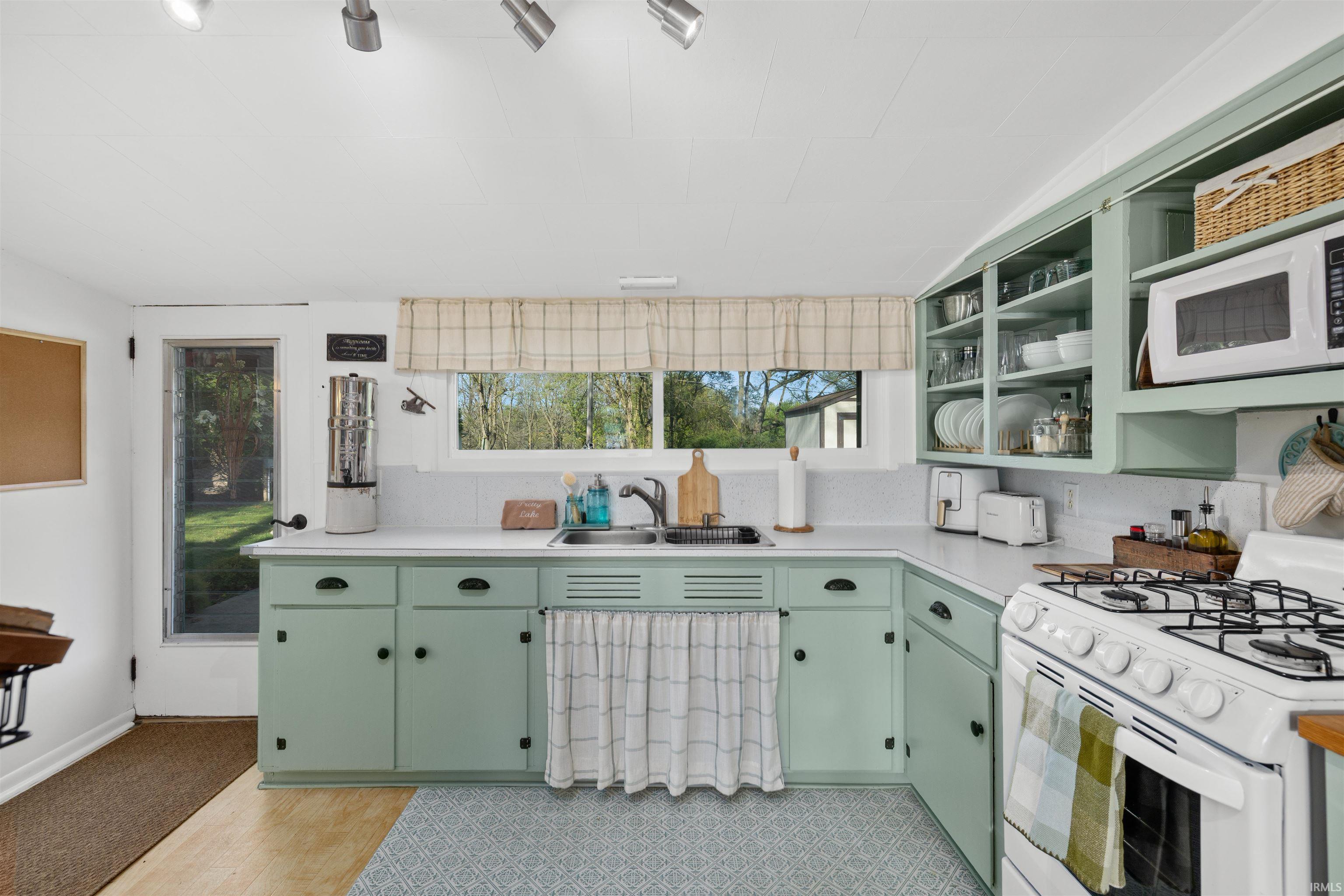 Kitchen featuring mint green cabinetry, white countertops, white tile backsplash, and a gas range