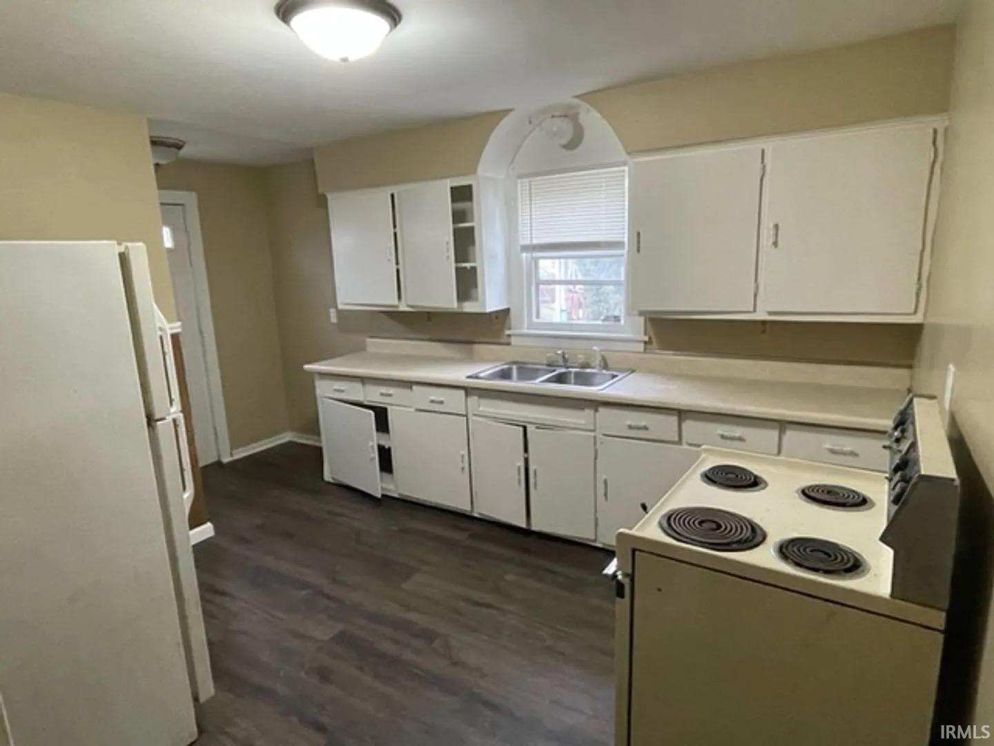 Kitchen featuring wood-finish flooring, white cabinetry, a double basin sink, and laminate countertops