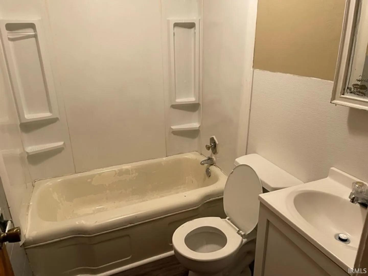 Bathroom featuring a white bathtub with integrated shelving, a classic white toilet, and a vanity with an integrated sink