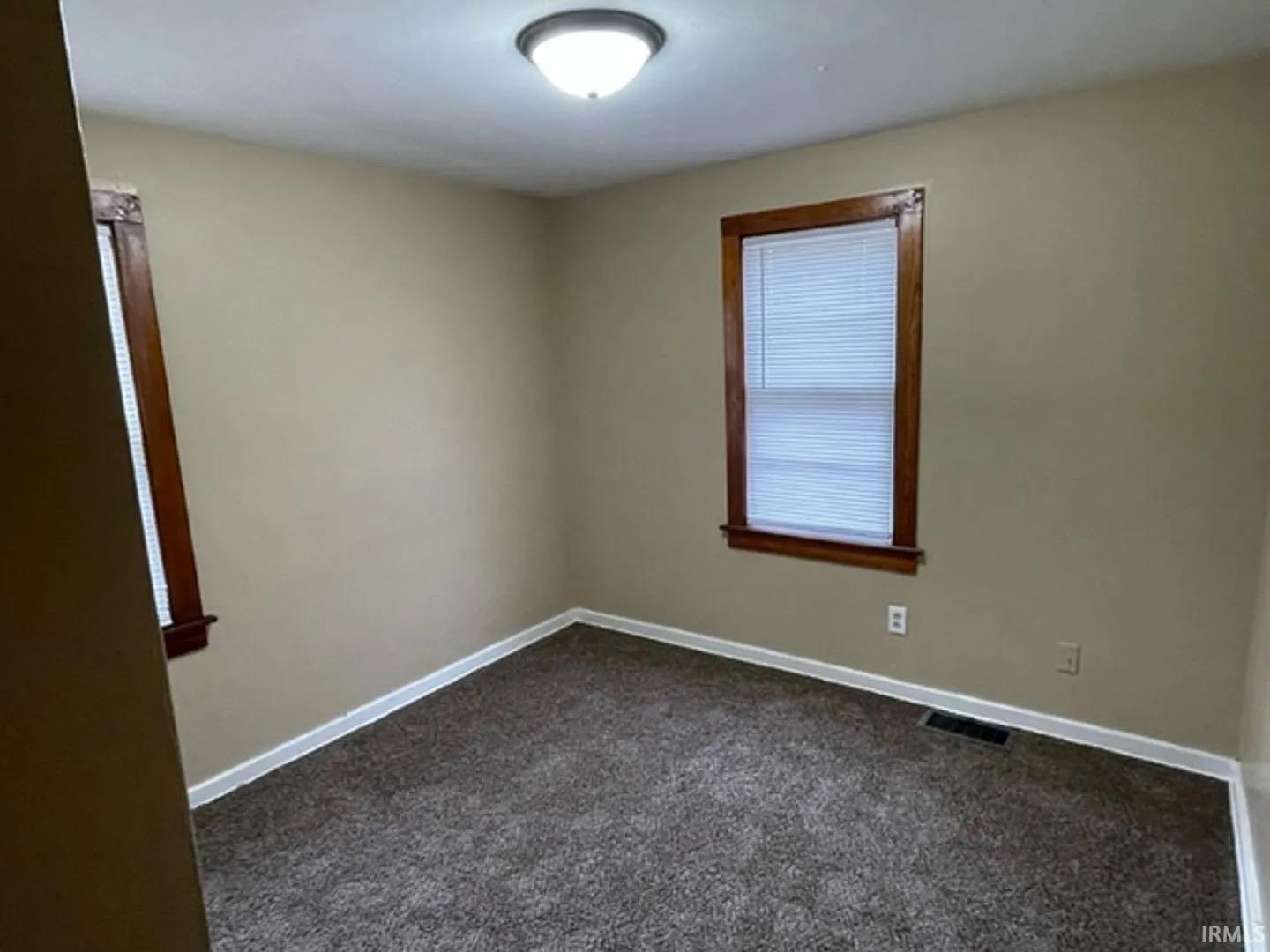 Carpeted room featuring neutral wall tones, two windows with wood trim, and a flush-mount ceiling light
